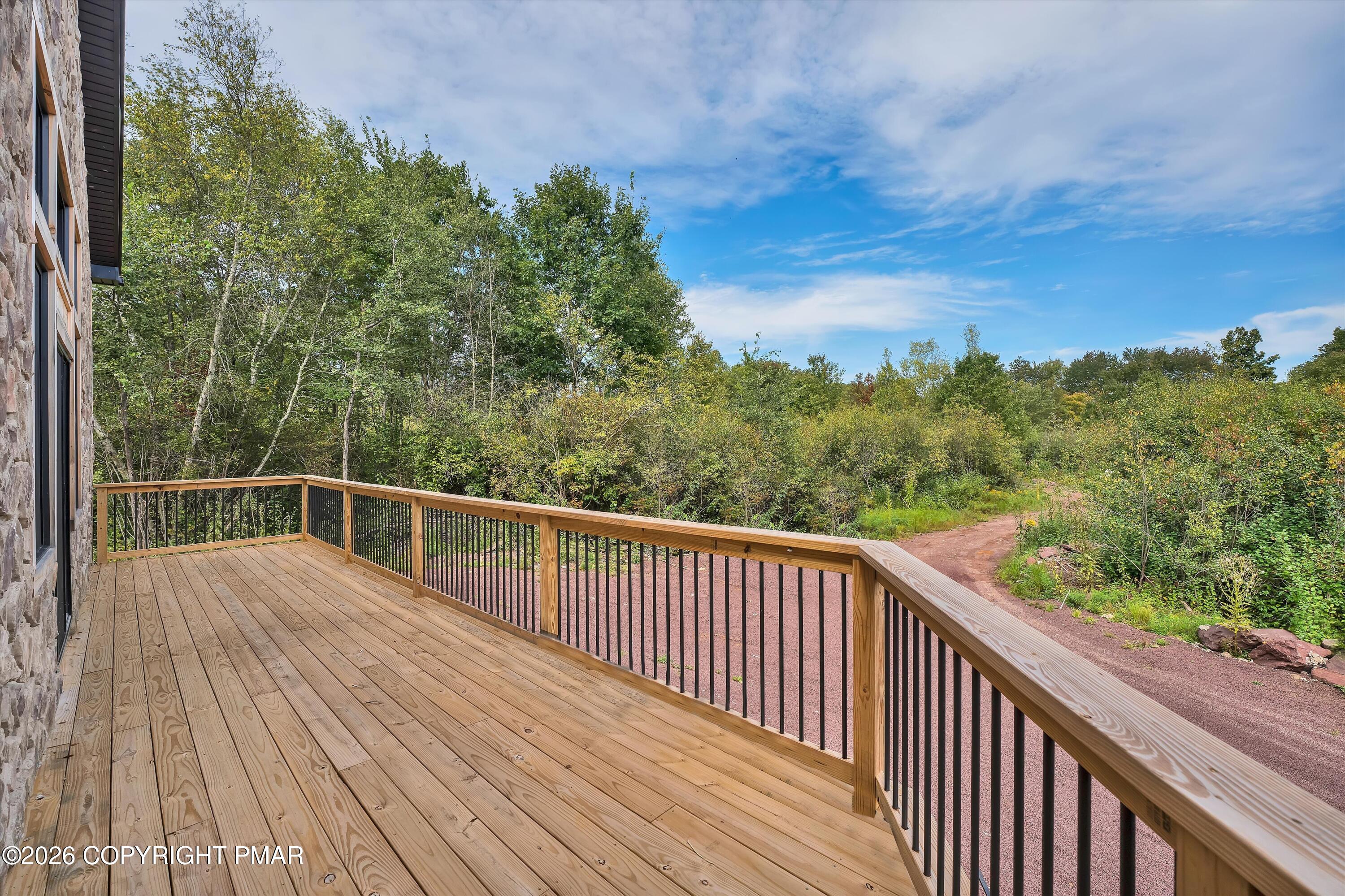 Wooden deck with black metal balusters overlooking trees and a reddish gravel drive.