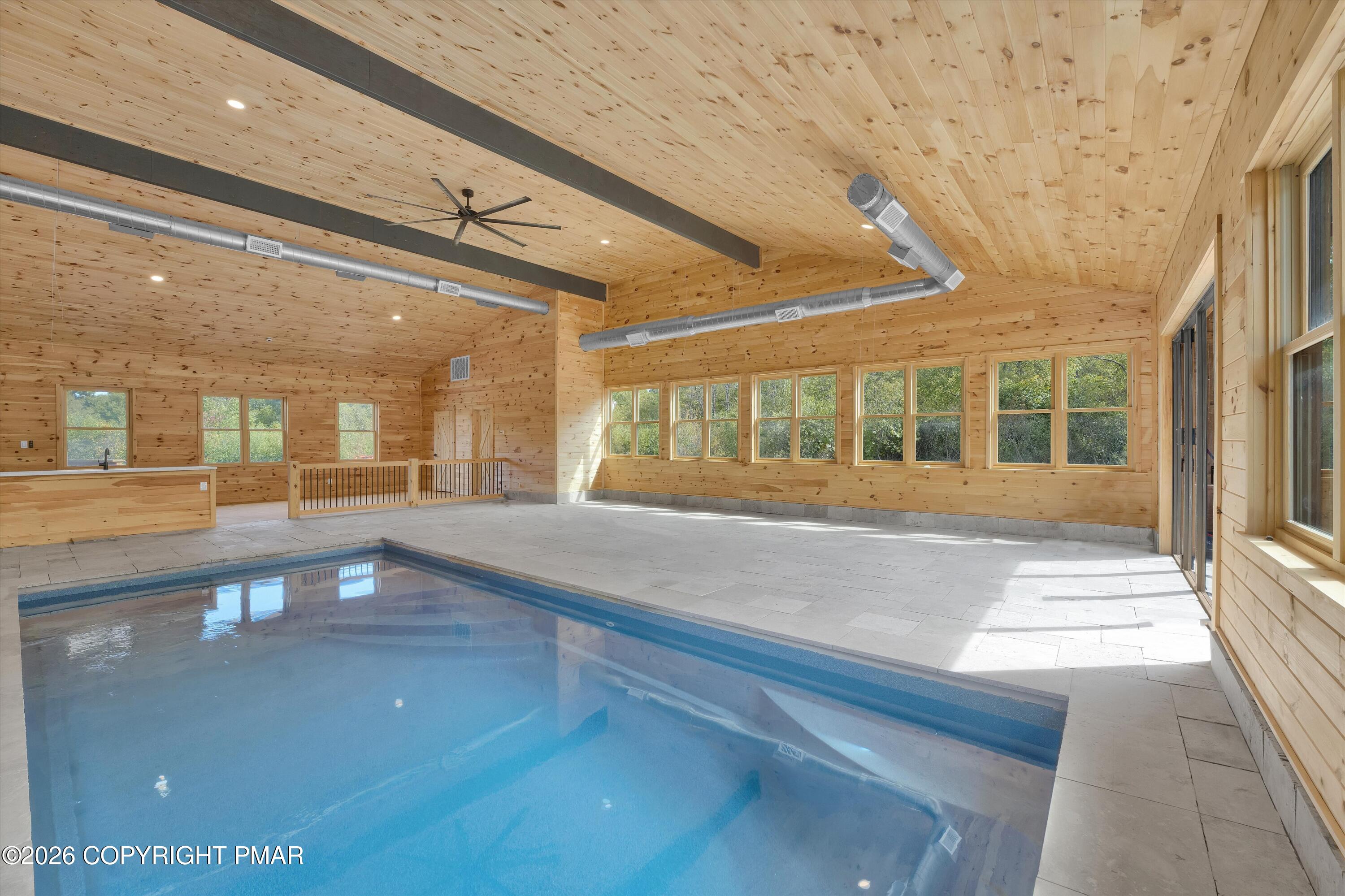 Indoor swimming pool in a wood-paneled room with large windows and pale tile flooring.