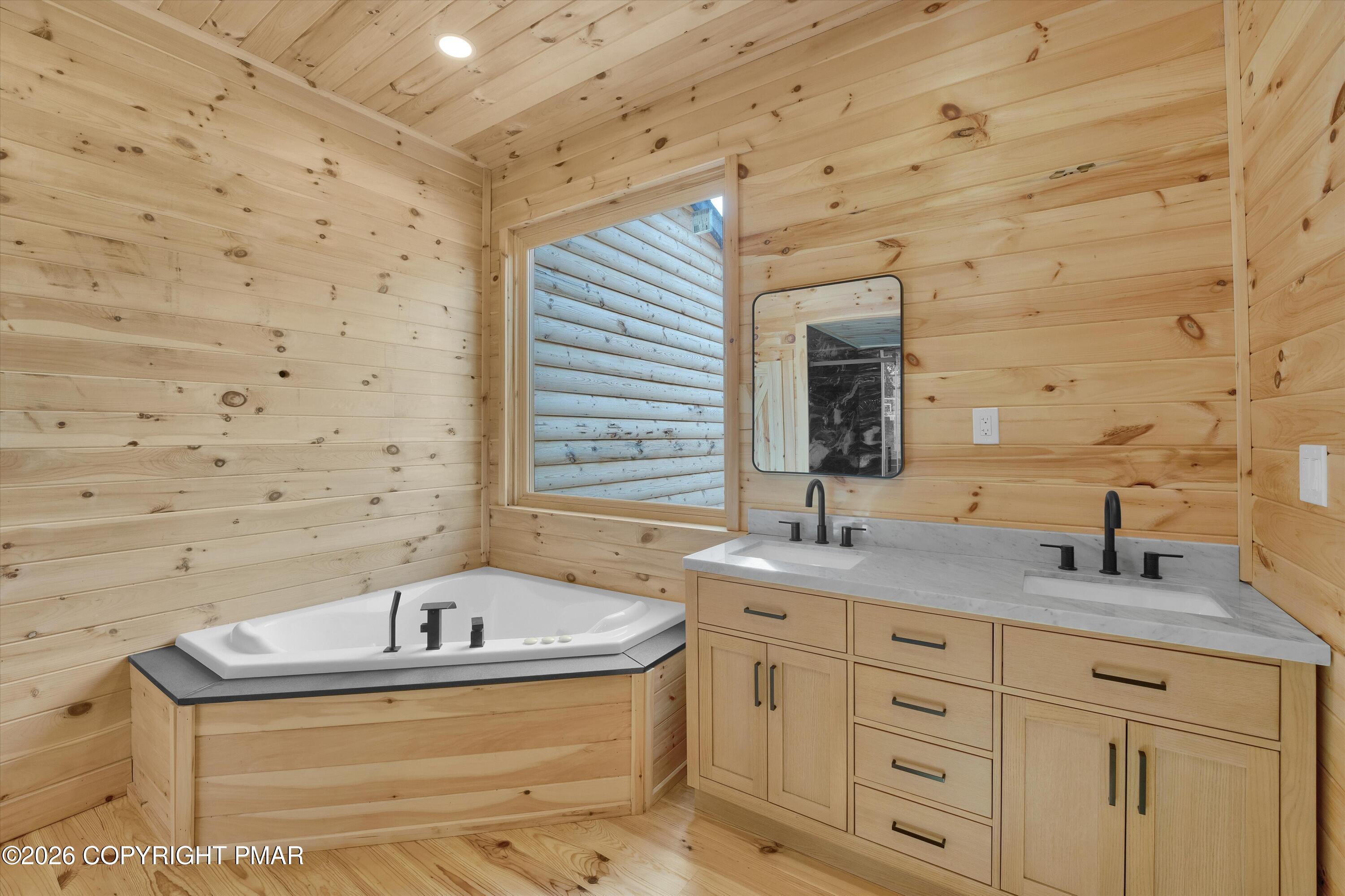 Wood-paneled bathroom with a soaking tub and double vanity beneath a black-framed mirror.