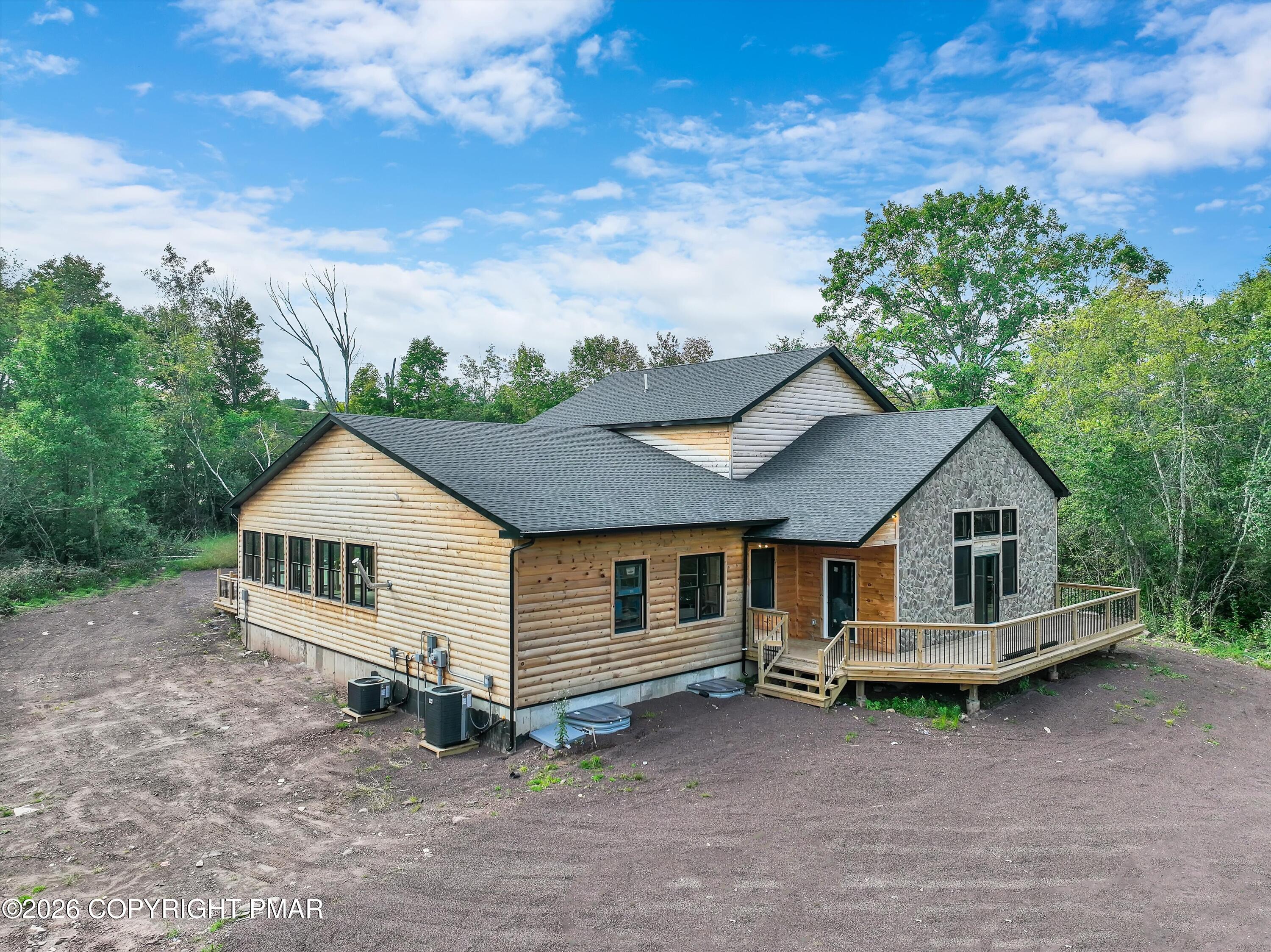 Log-sided home with a stone-faced gable and raised wood deck on a wooded lot.