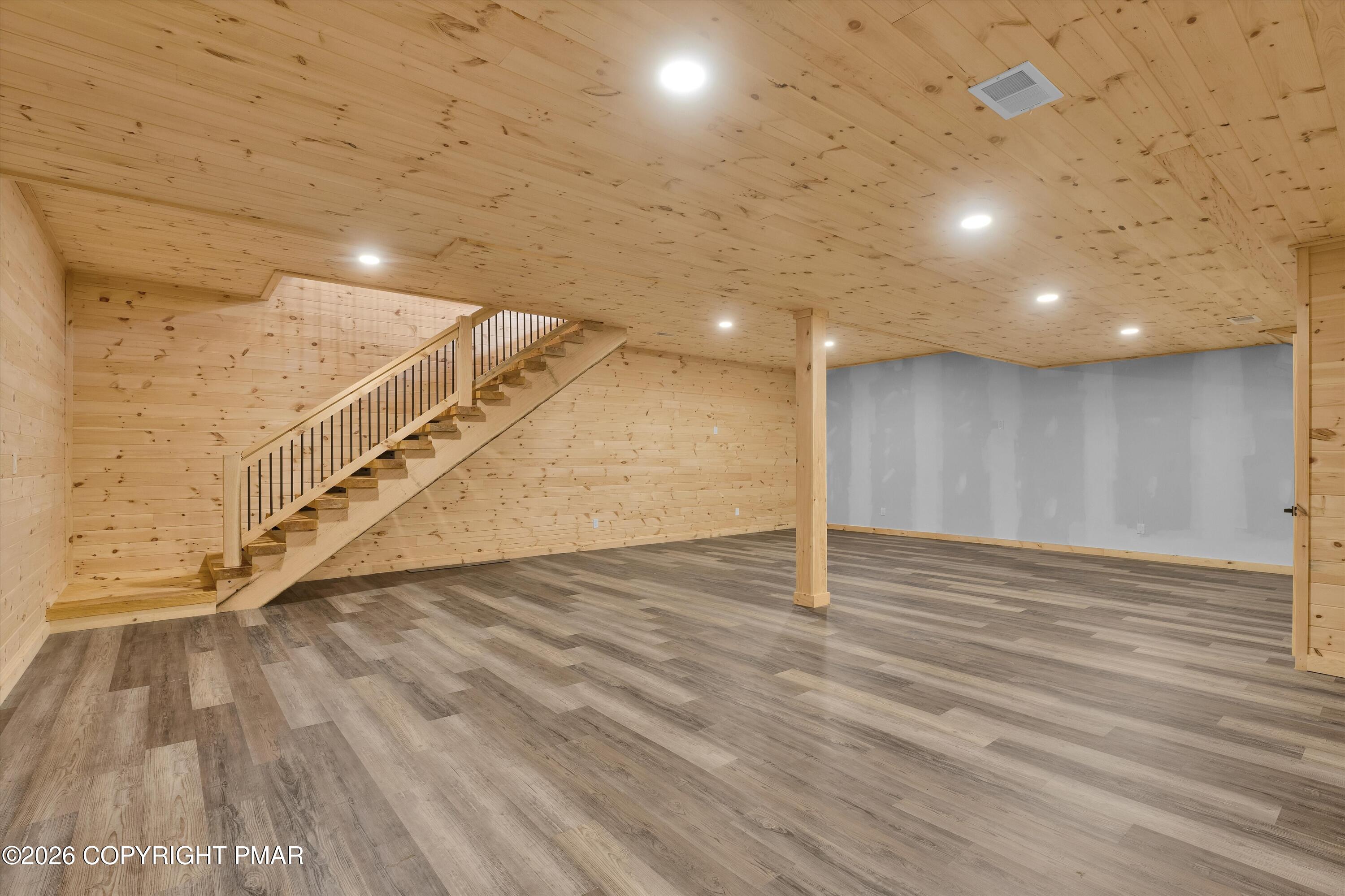 Finished basement with wood-plank walls and ceiling, open floor, and staircase with dark metal balusters.