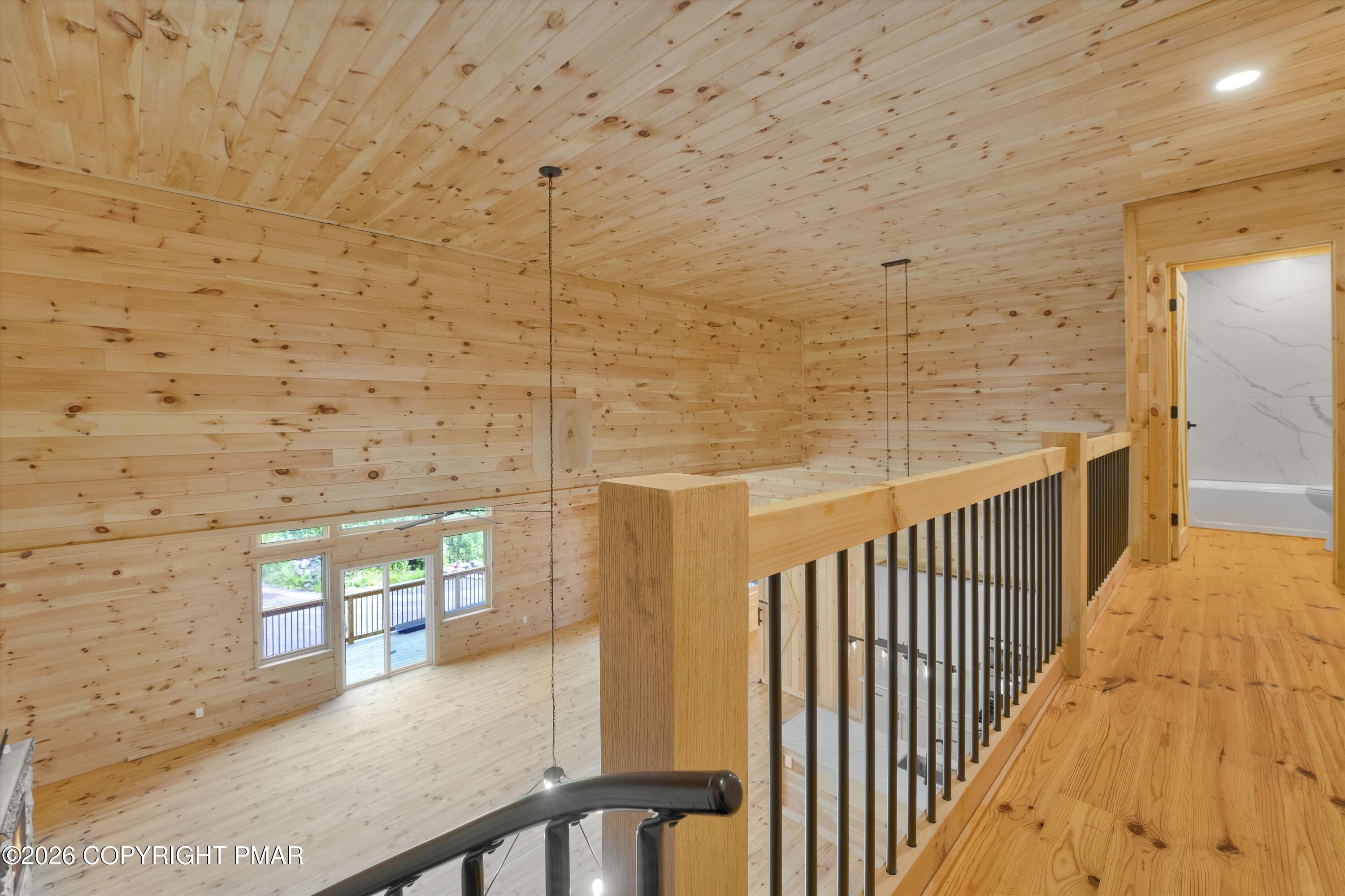 Wood-paneled upper landing with black metal railing overlooking a bright, double-height room.