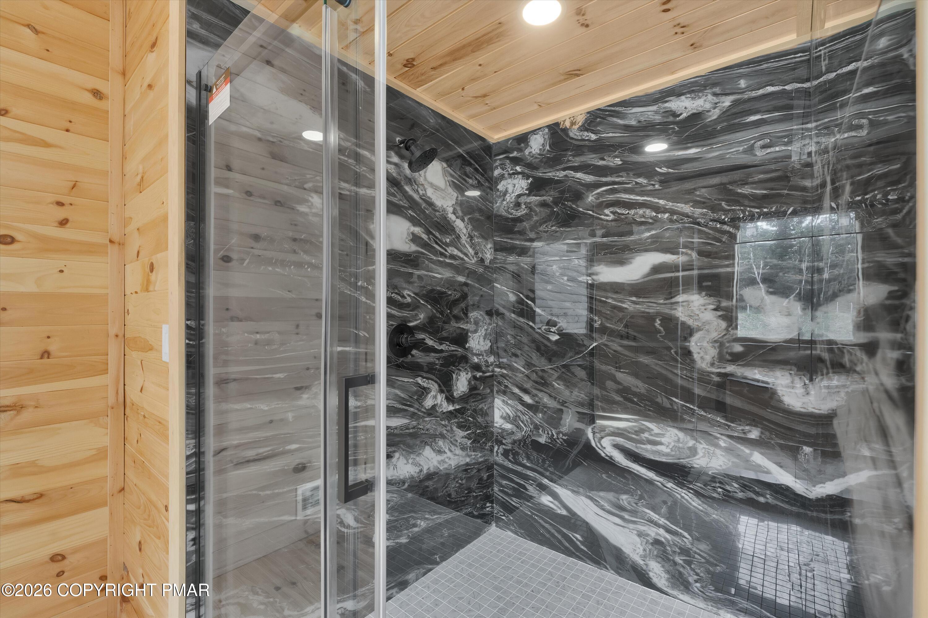 Glass-enclosed shower with bold black and white veined tile and a wood-plank ceiling.
