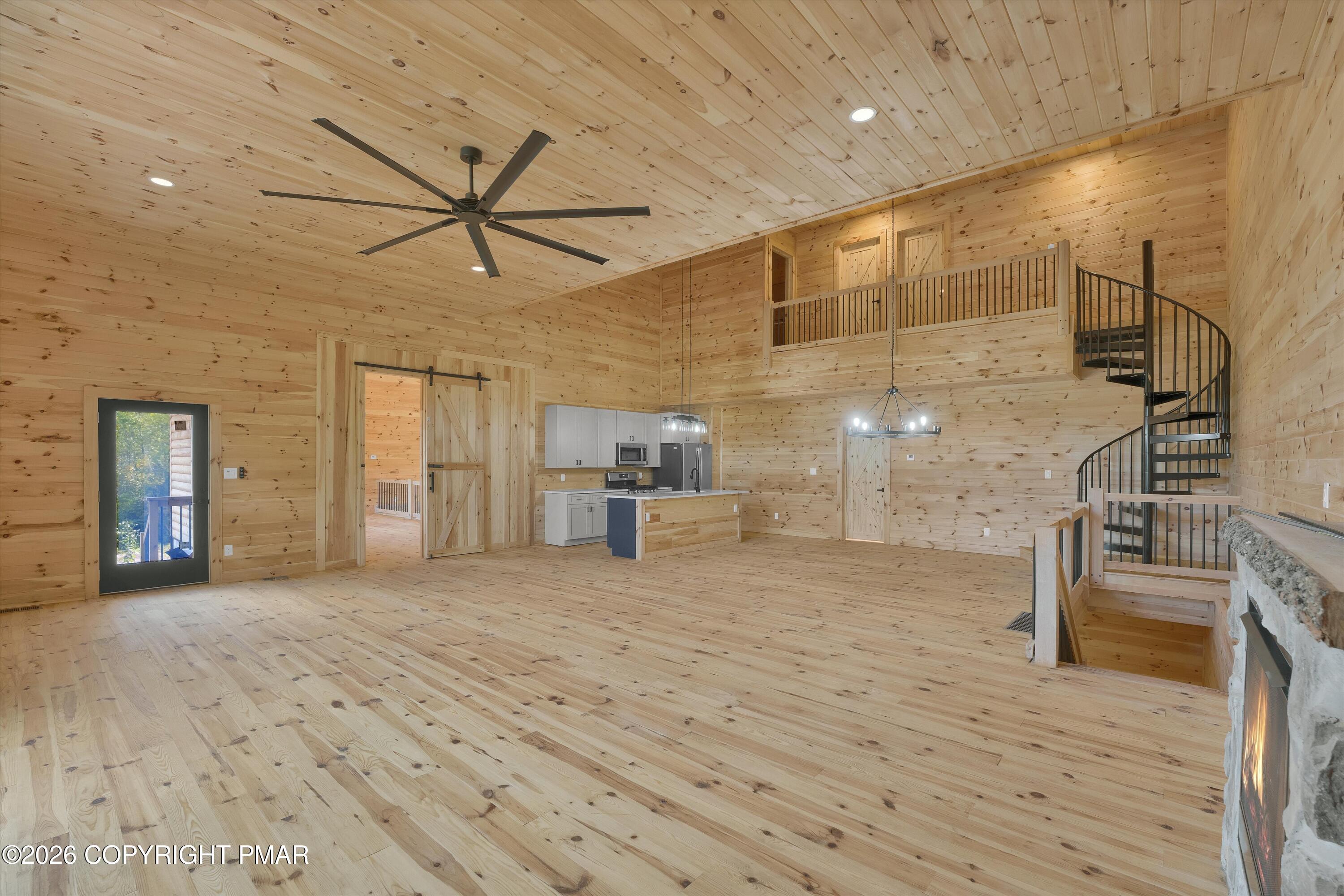Vacant pine-paneled great room with an open kitchen, spiral staircase, and stone fireplace.