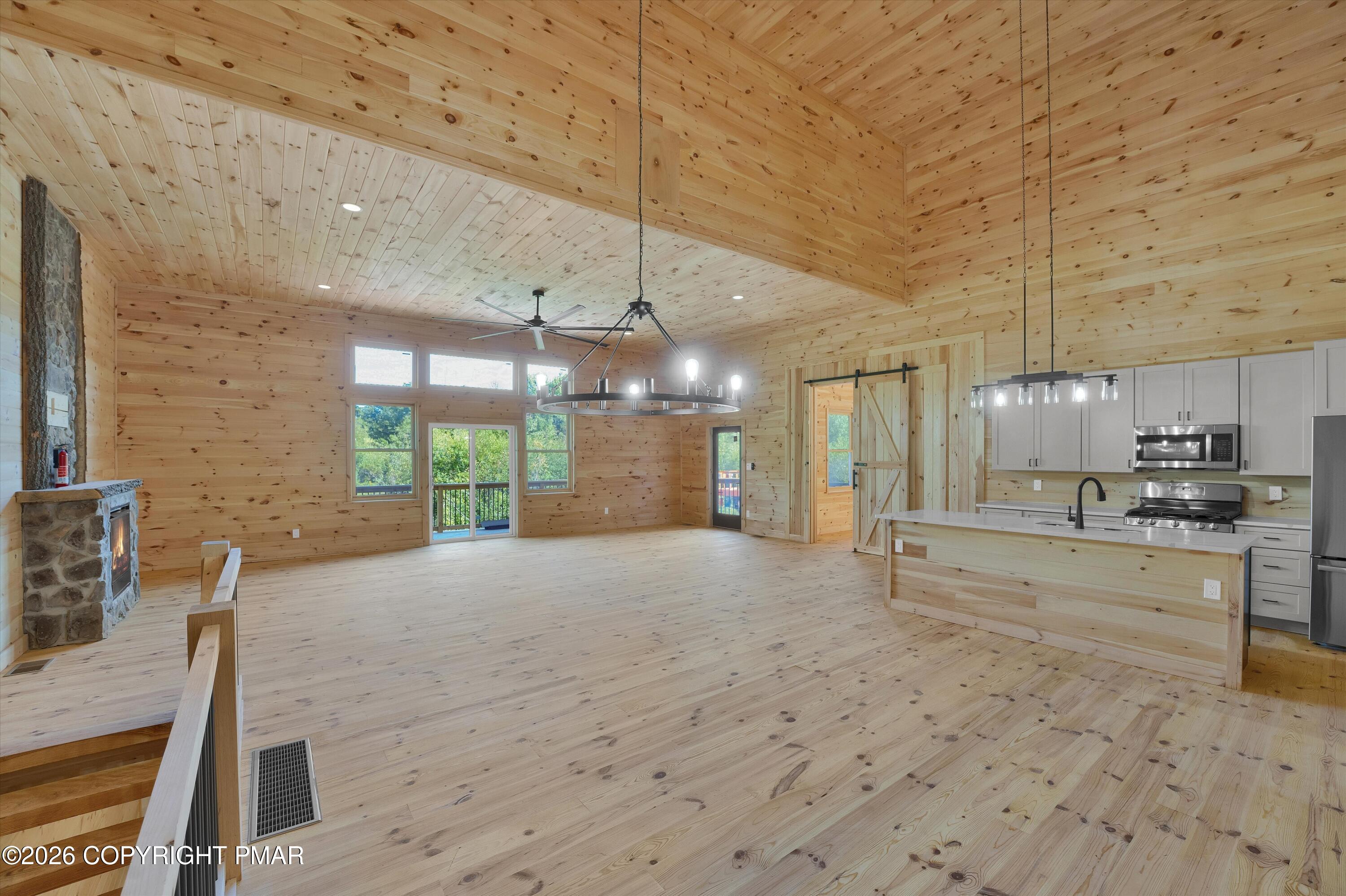 Open-plan living room and kitchen with vaulted pine ceilings, stone fireplace, and large island.