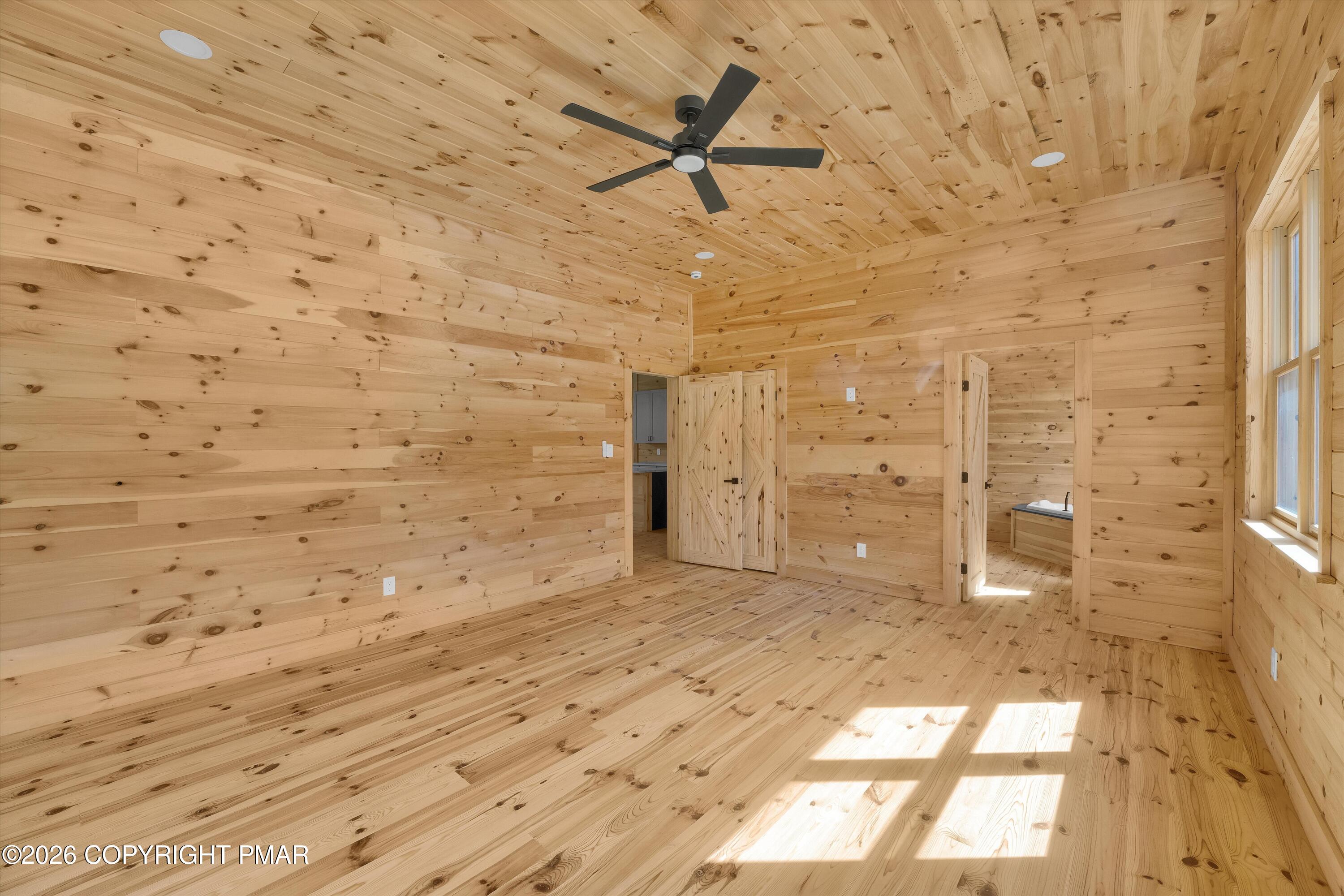 Empty wood-paneled room with a black ceiling fan and sunlight streaming through tall windows.