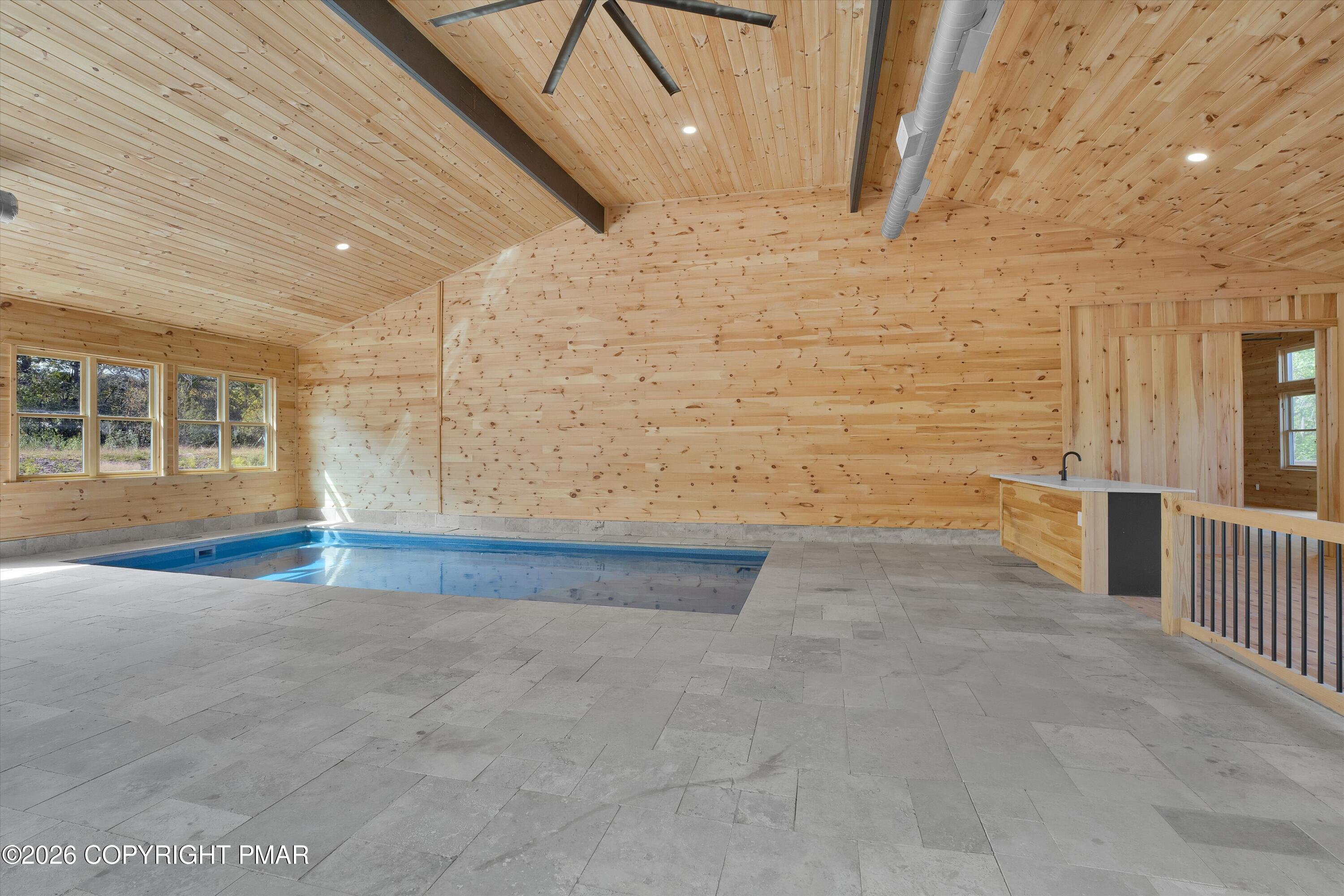 Indoor swimming pool in a vaulted wood-paneled room with gray tile flooring and large windows.