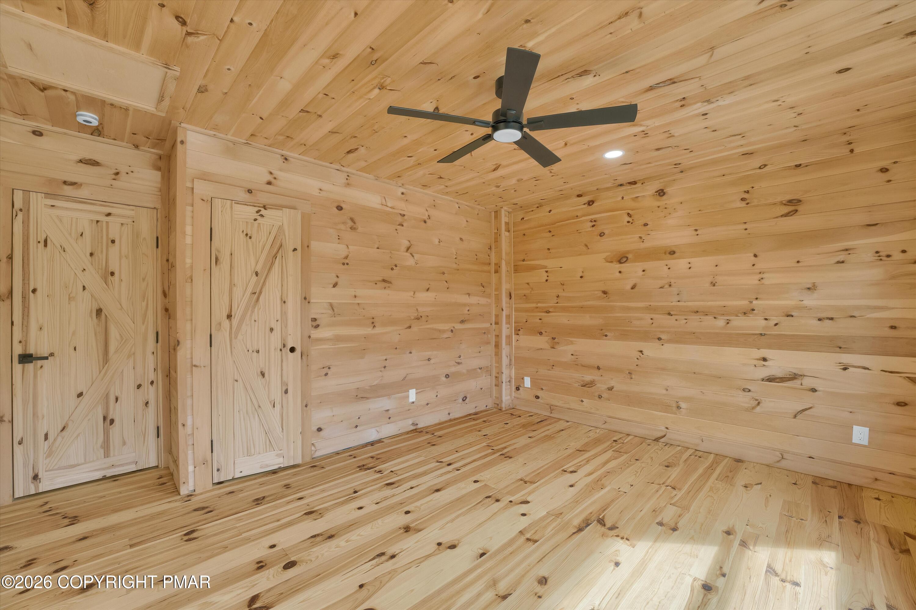 Empty knotty-pine room with two barn-style doors and a black ceiling fan.