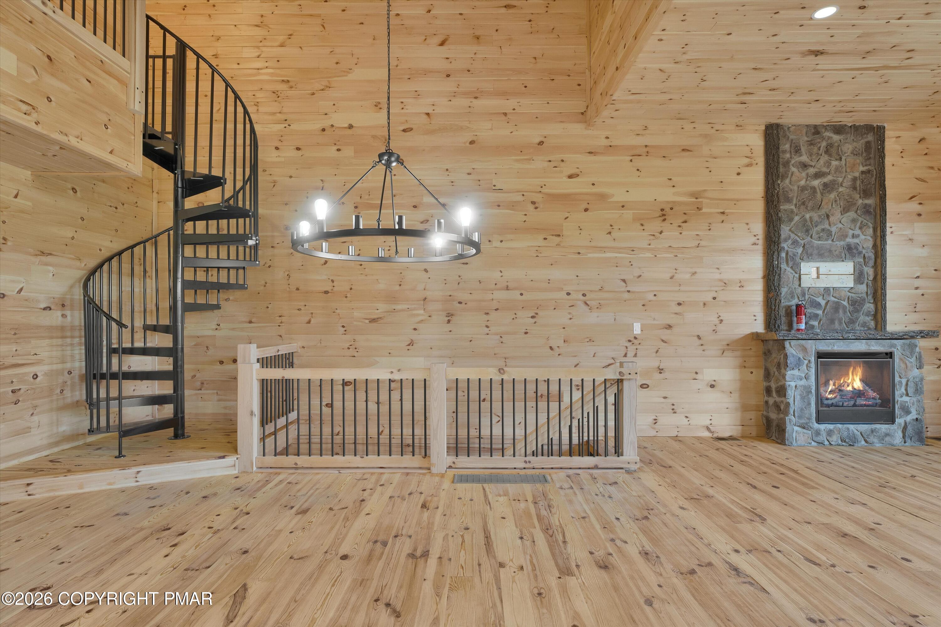 Wood-paneled great room with a spiral staircase, circular chandelier, and stone fireplace.