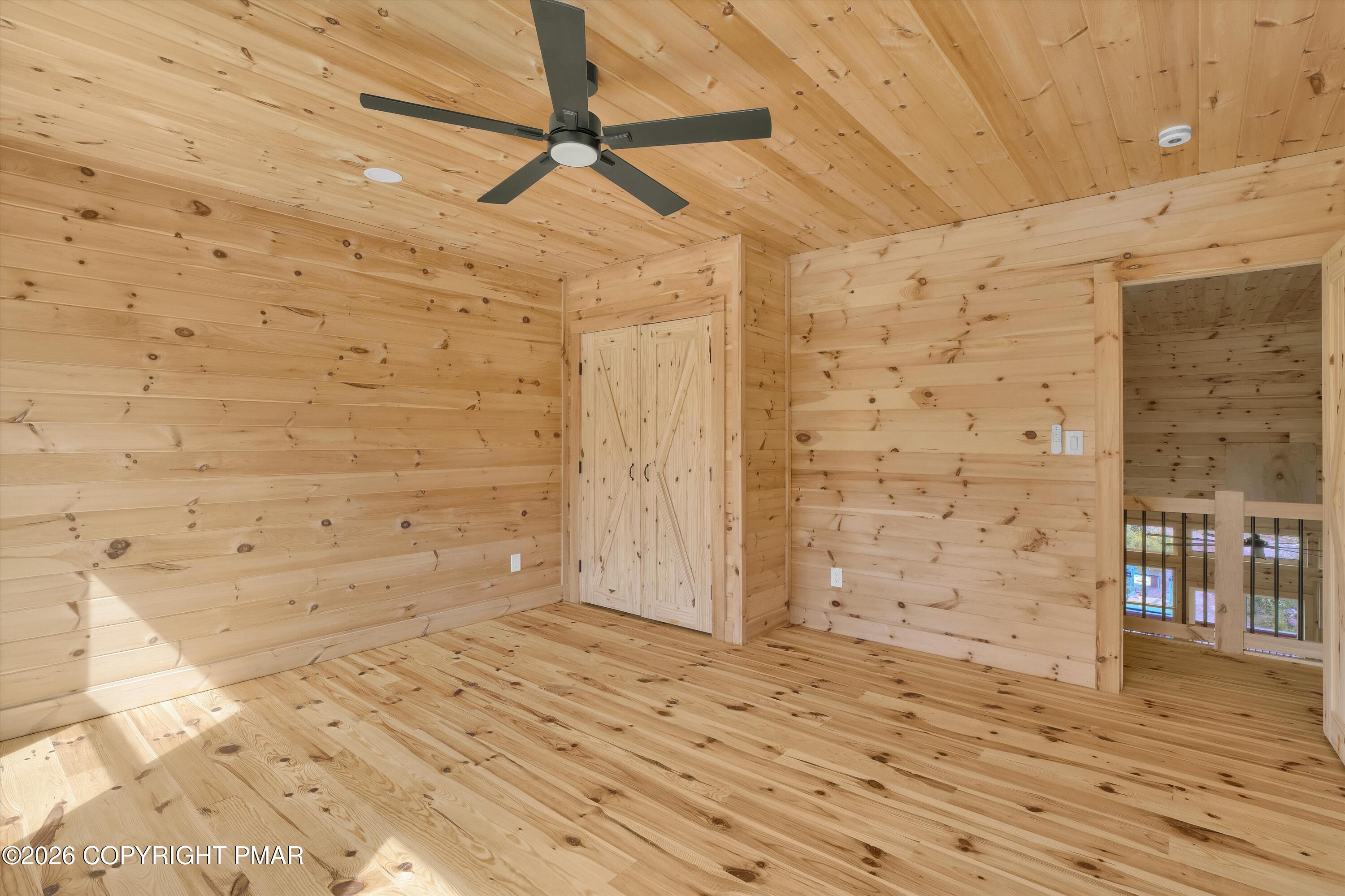Wood-paneled bedroom with a black ceiling fan, built-in closet, and open loft railing.