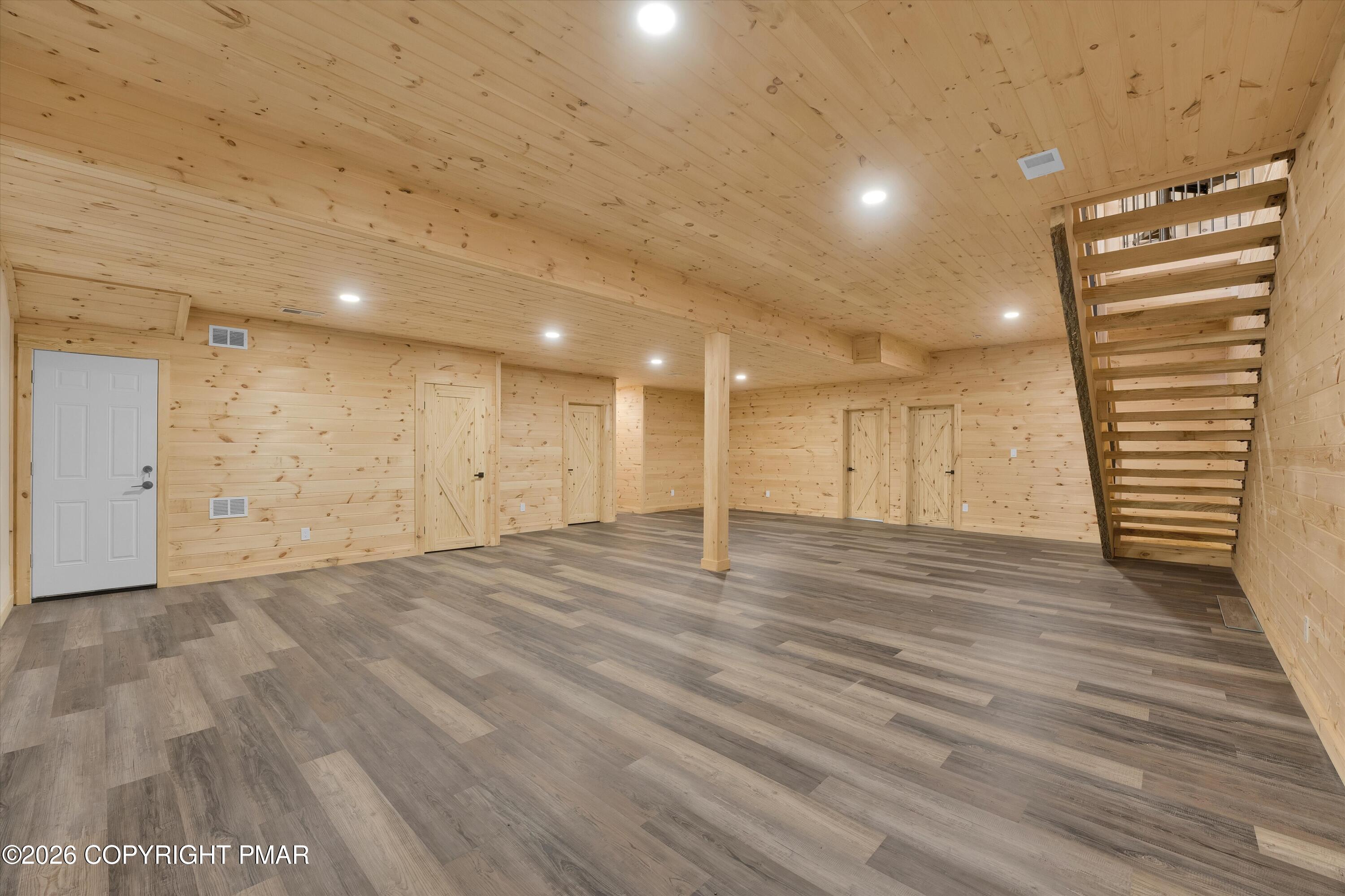 Vacant wood-paneled room with gray plank flooring and an open-riser staircase.