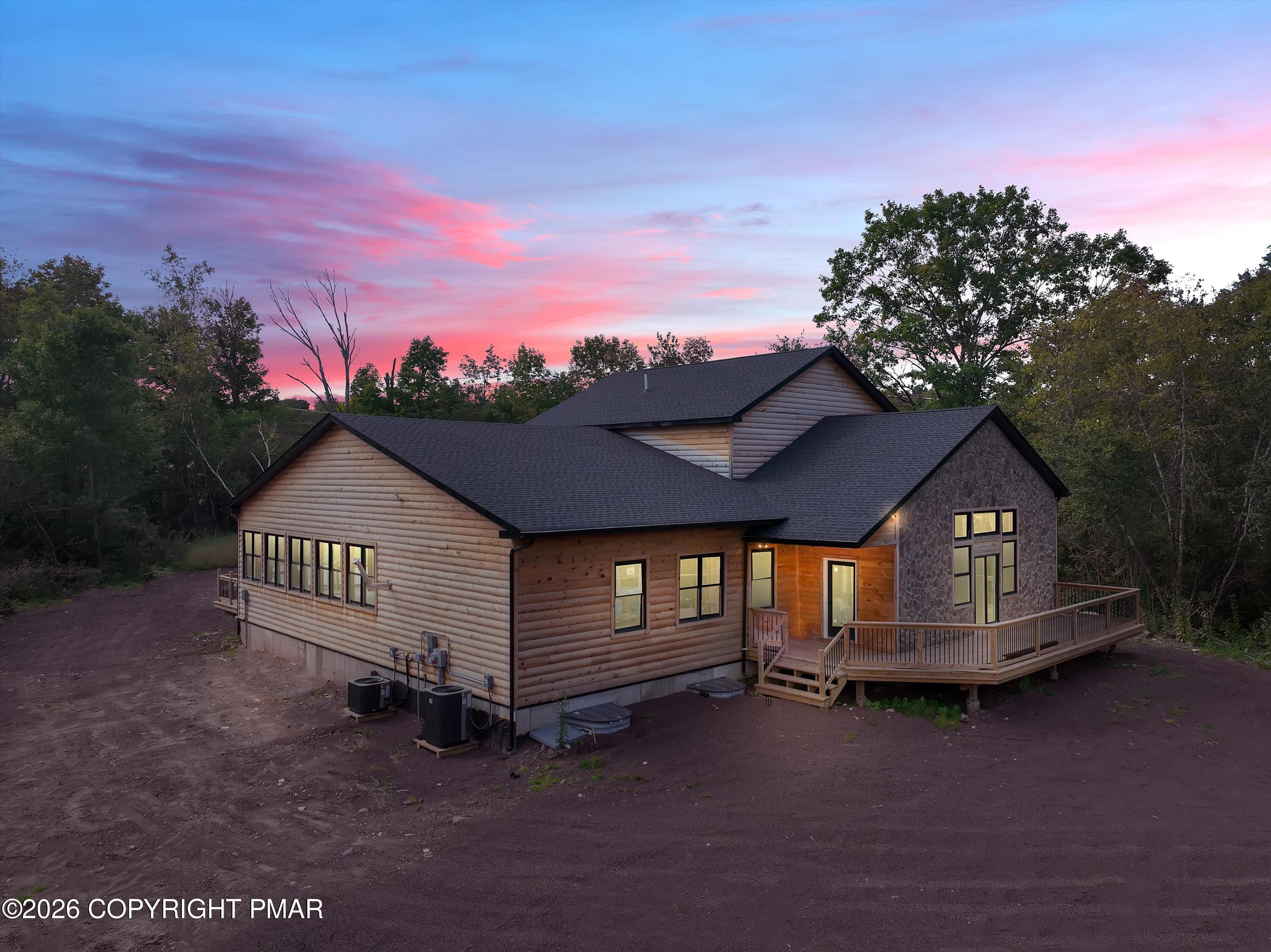 Log-sided home with stone facade and raised deck beneath a pink dusk sky.