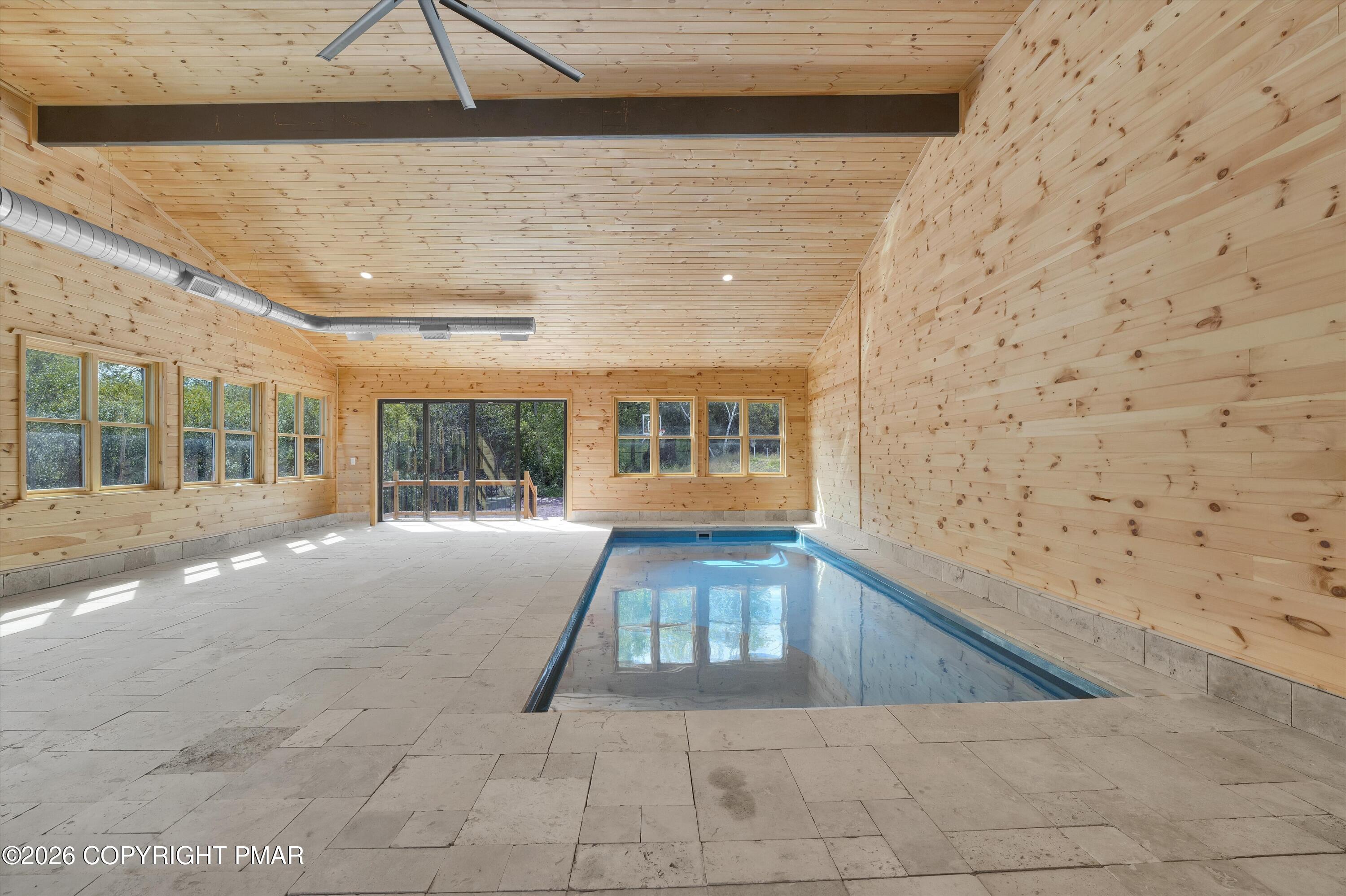 Indoor swimming pool in a wood-paneled room with large windows and pale tile flooring.