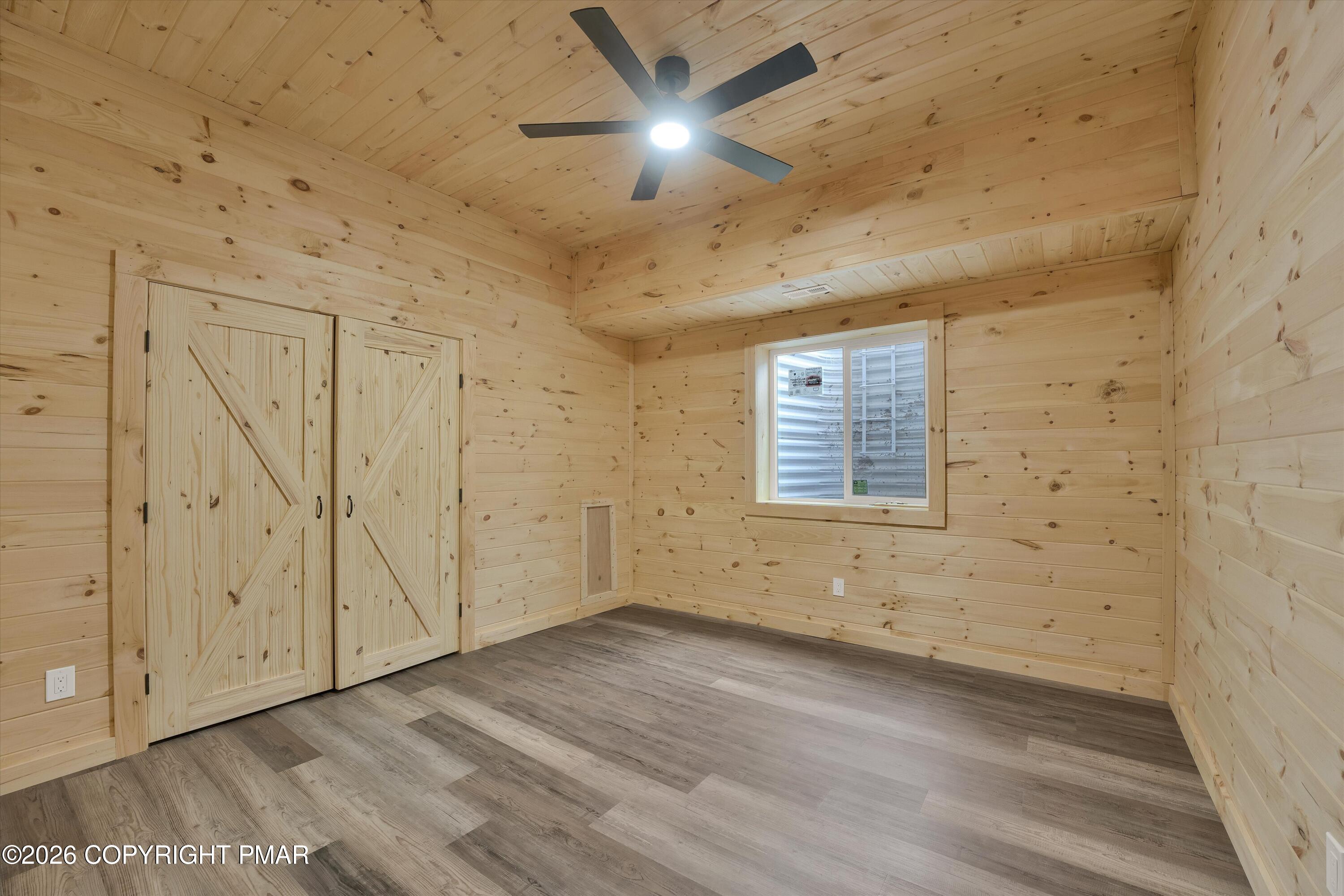 Empty pine-paneled room with gray flooring, barn-style closet doors, a window, and ceiling fan.