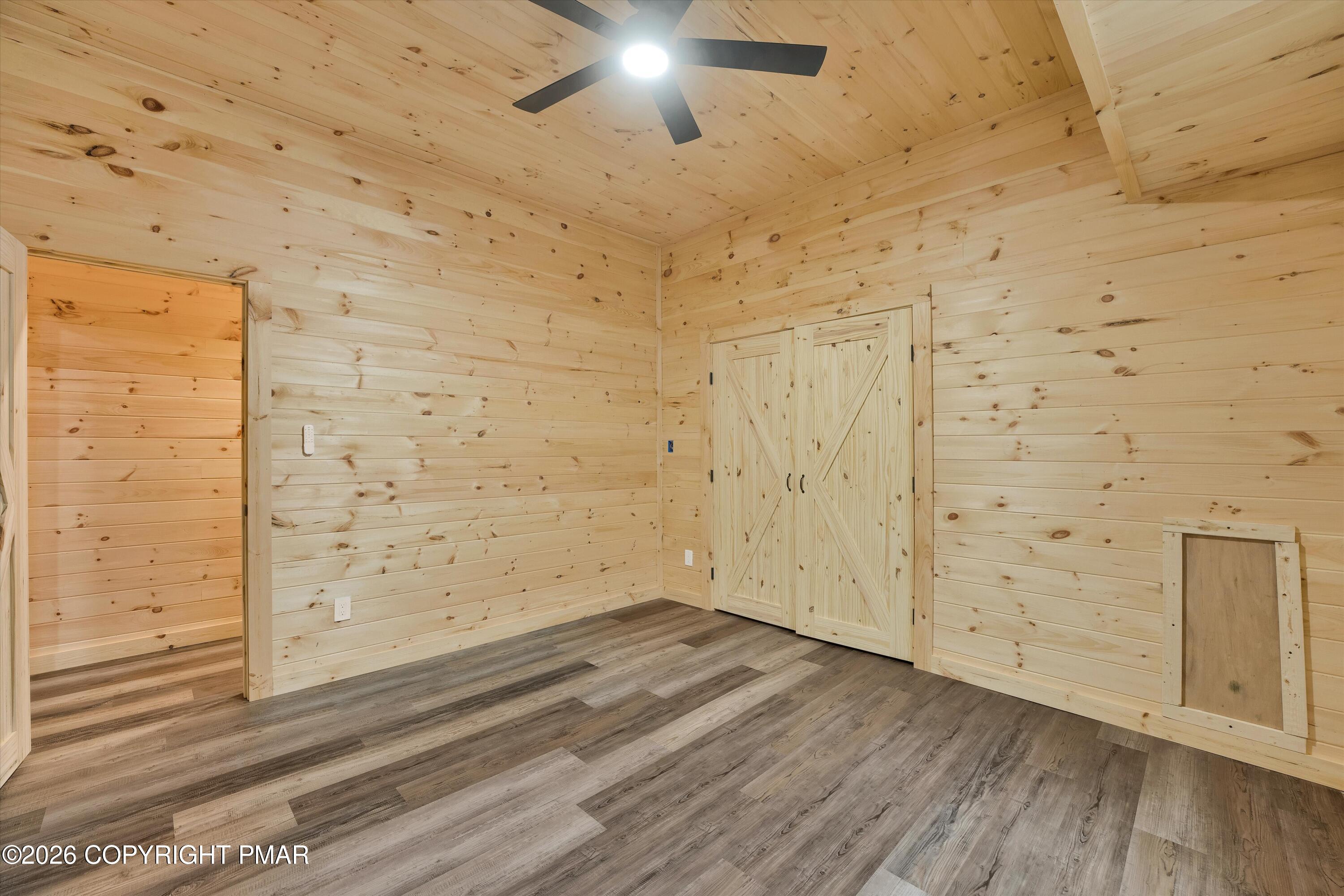Vacant wood-paneled room with gray plank flooring, ceiling fan, barn-style closet doors, and a pet door.