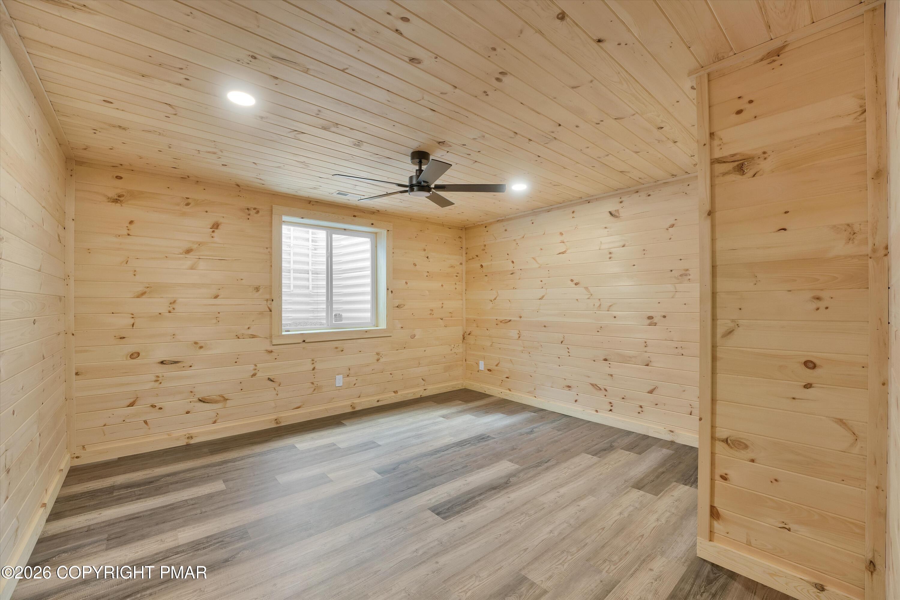 Empty room with natural-wood plank walls and ceiling, gray flooring, a ceiling fan, and a window.
