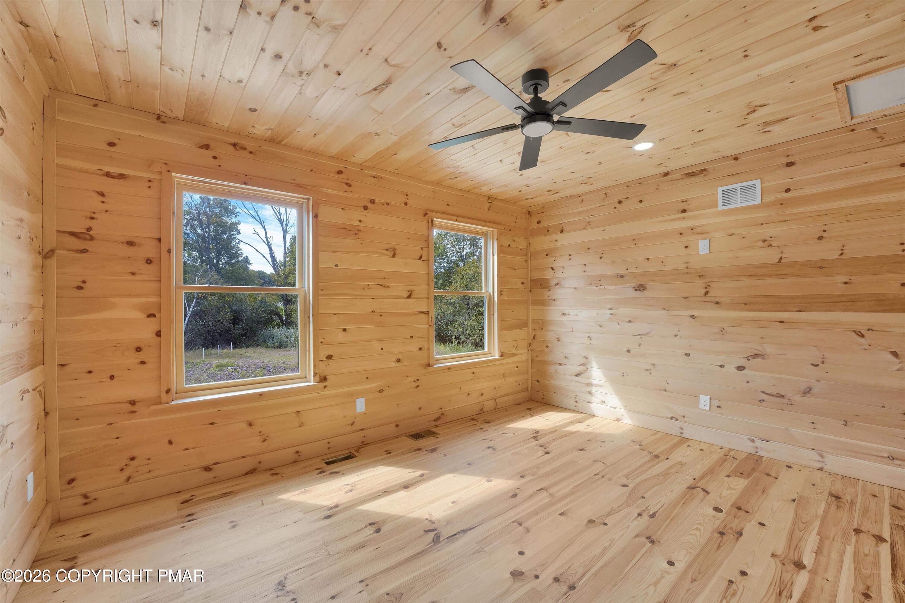 Empty knotty-pine room with two windows, wood flooring, and a ceiling fan.