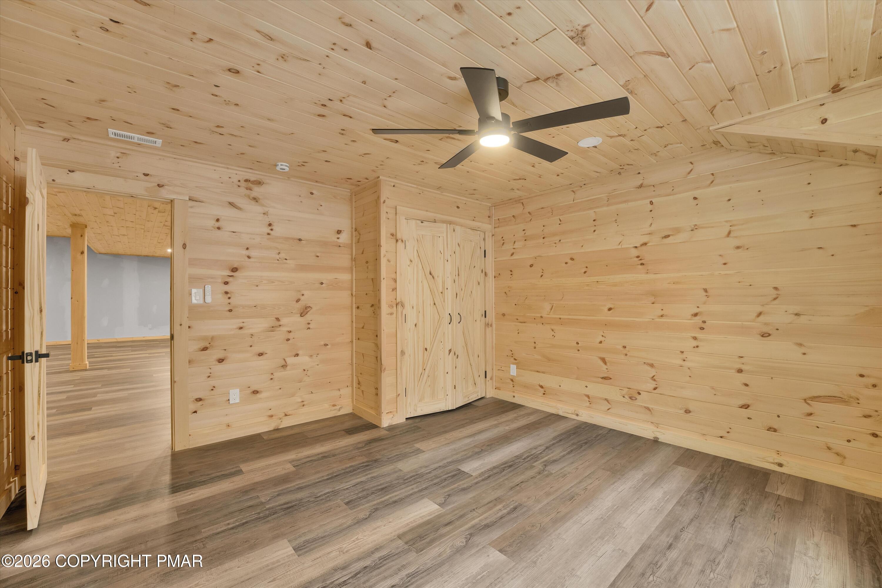Empty pine-paneled room with a black ceiling fan and double barn-style closet doors.