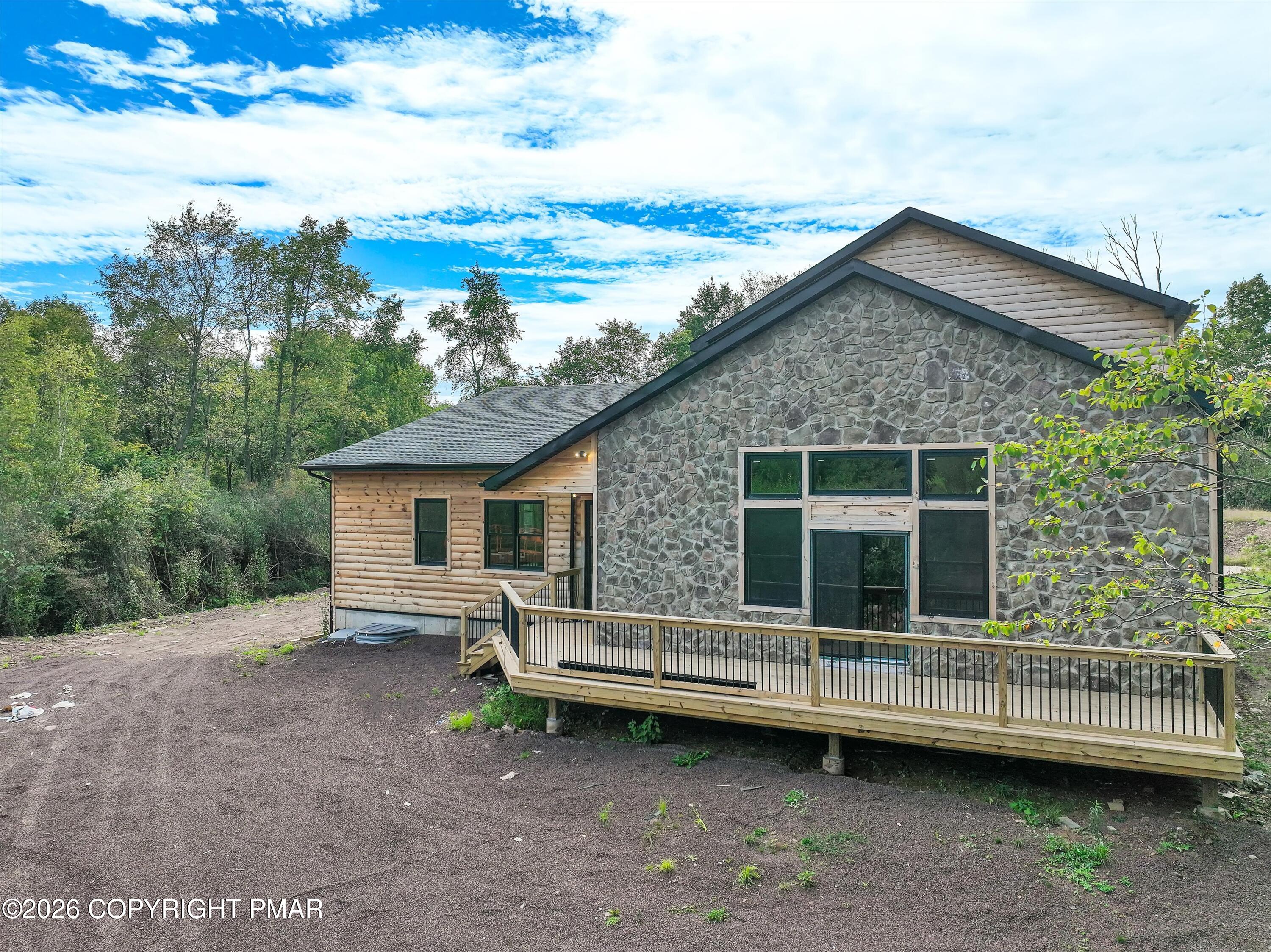 House with a stone facade, wood siding, and an elevated deck surrounded by trees.