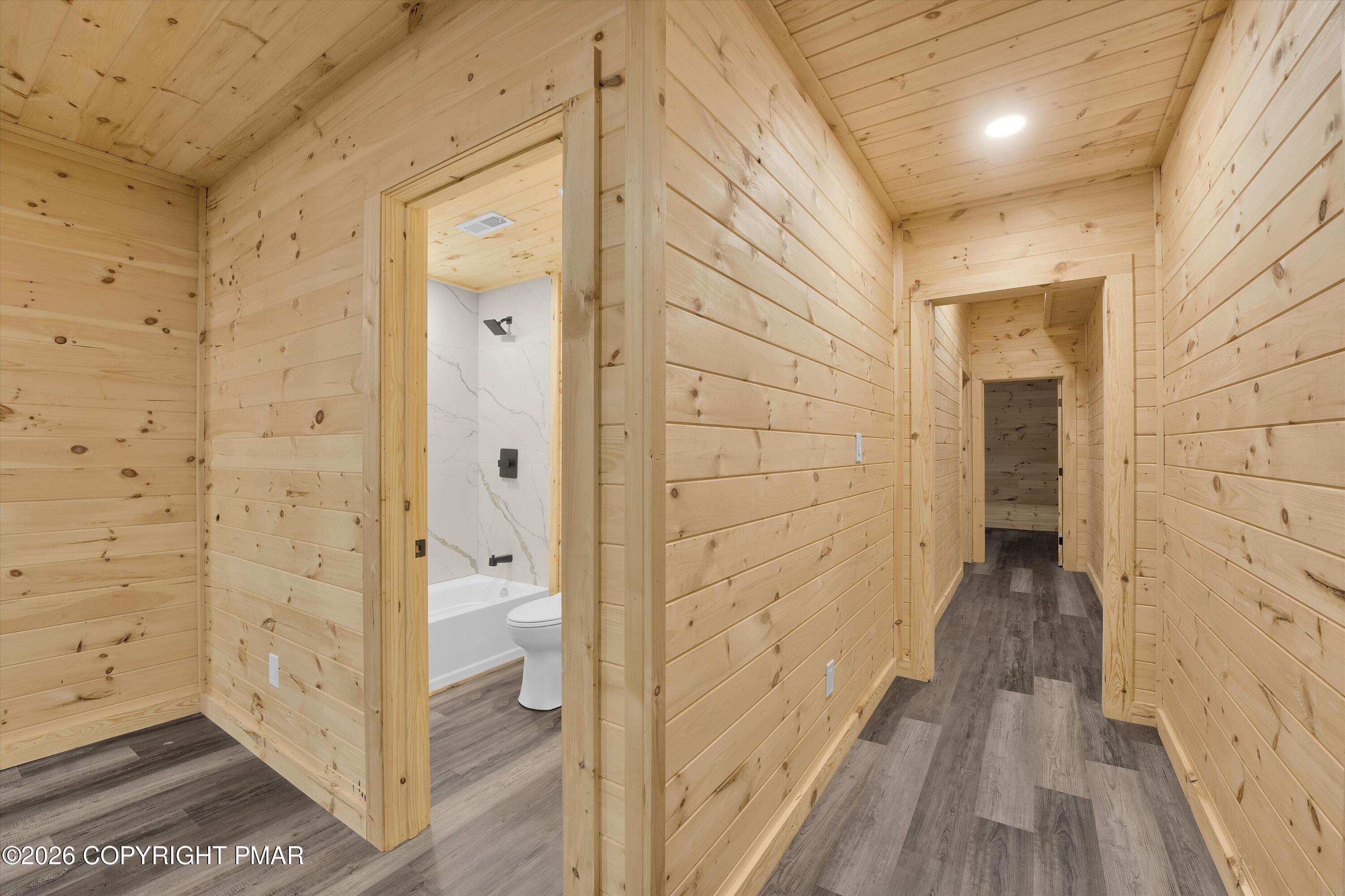 Wood-paneled hallway with gray plank flooring and an open doorway to a bathroom.