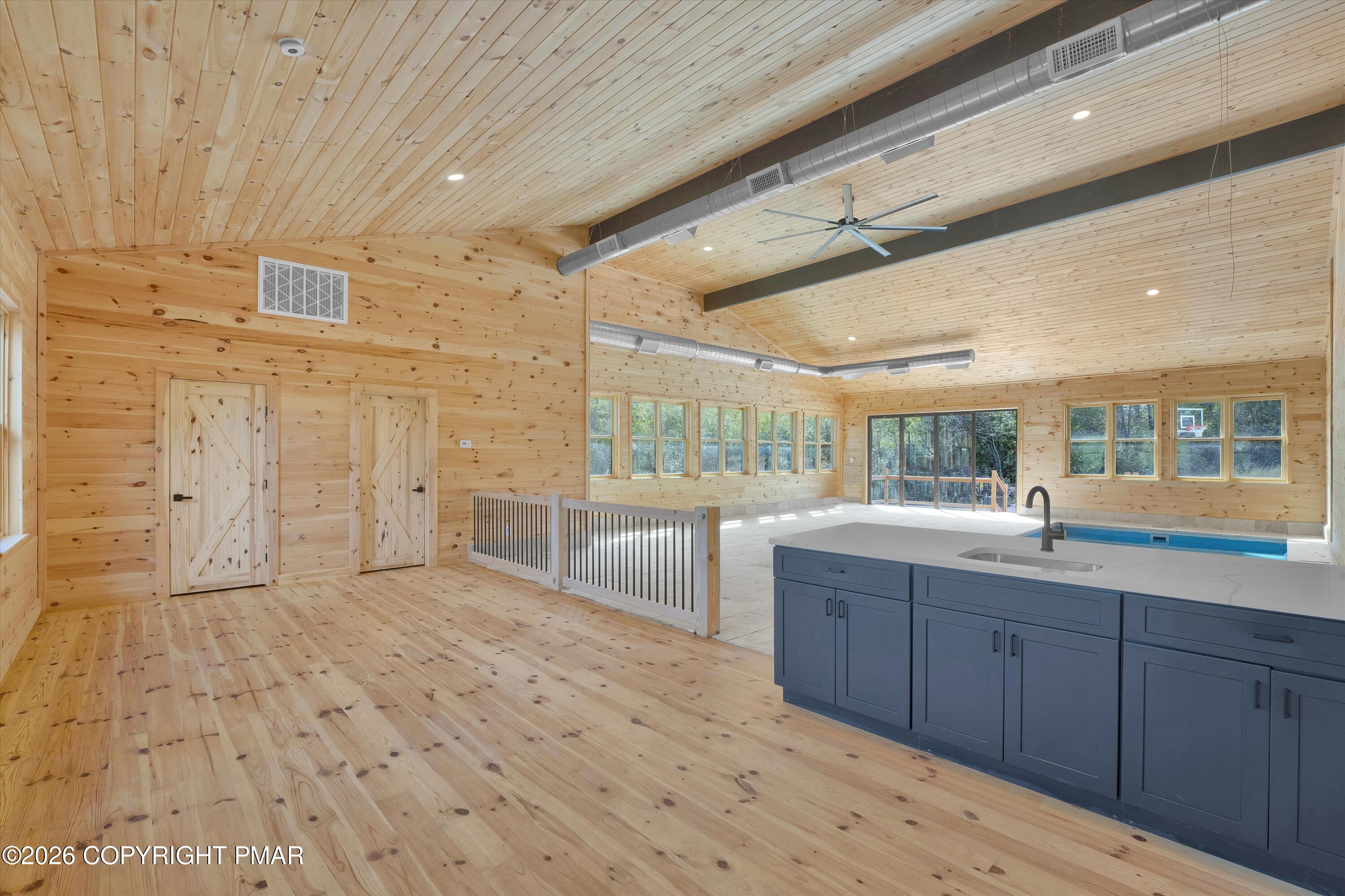 Indoor pool room with pine paneling, a blue-gray island, and windows overlooking trees.