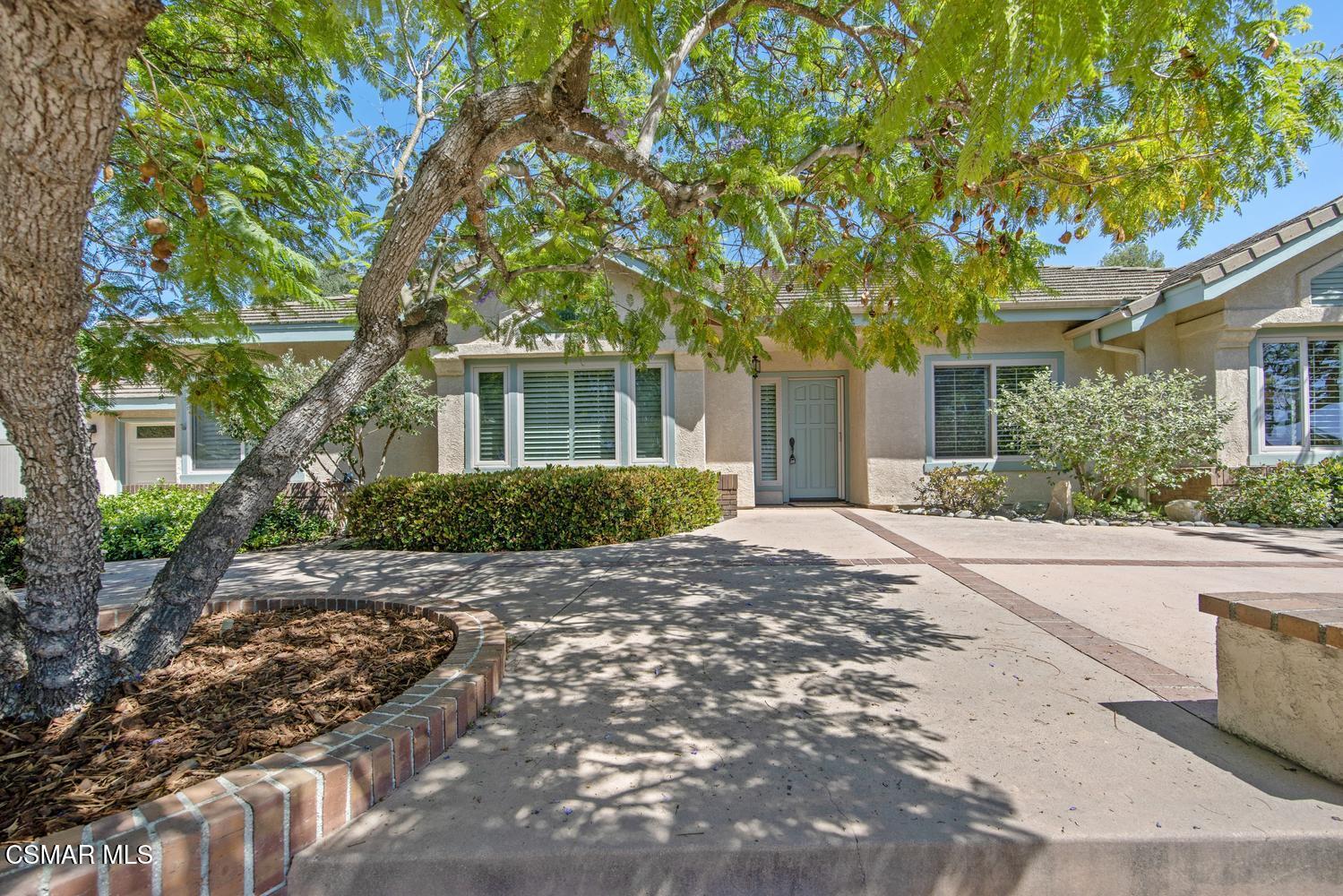 Single-story home with a blue-gray front door and a large tree shading the driveway.