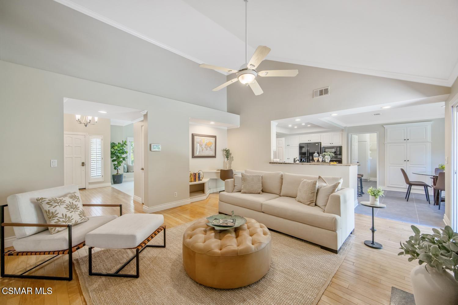 Open-plan living room with vaulted ceiling, cream seating, and a view into the white kitchen.