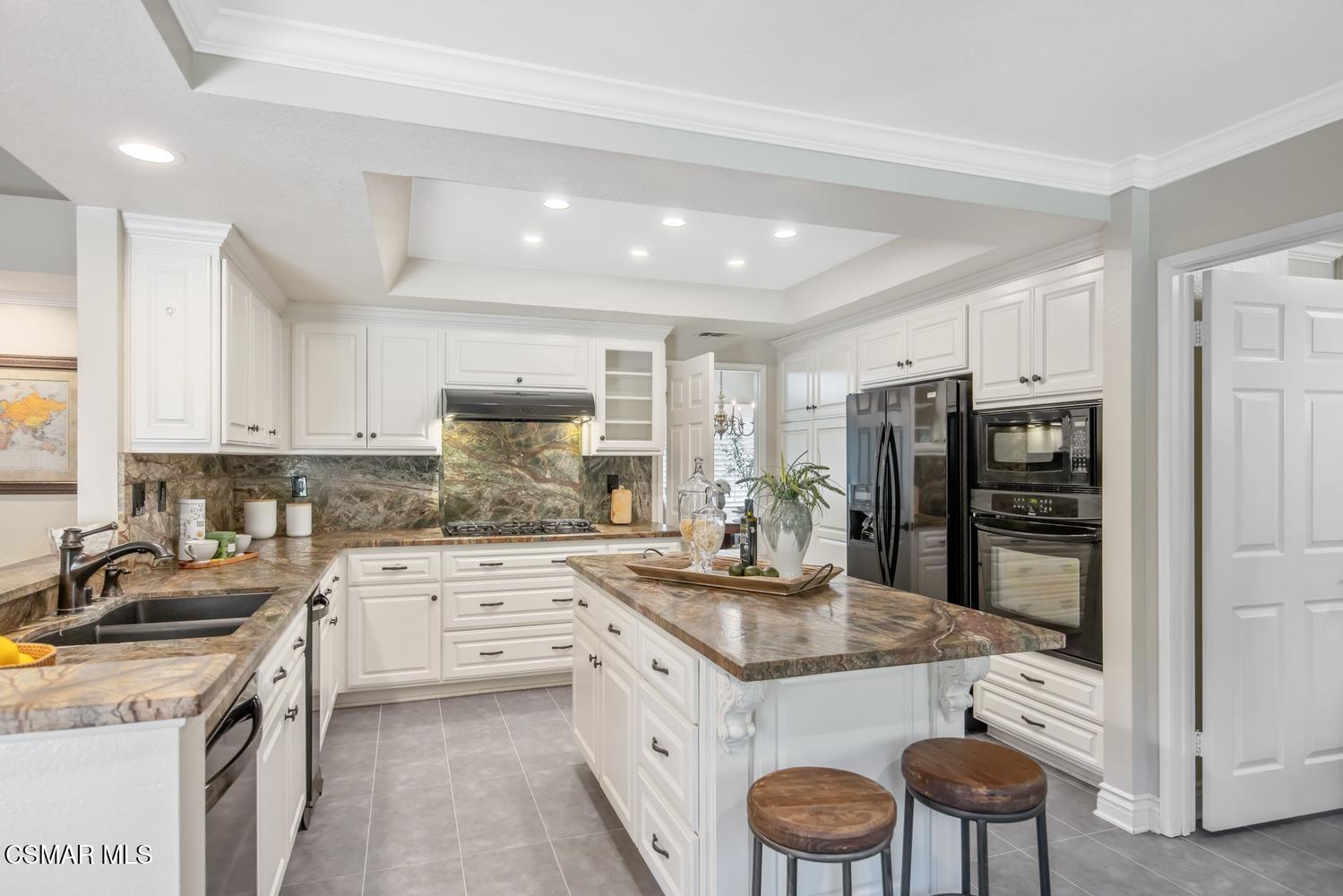 Kitchen with white cabinets, patterned stone counters, a large island, and two wooden stools.