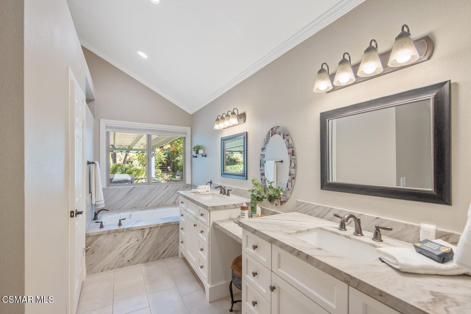 Primary bathroom with a long double vanity and a soaking tub beneath a garden-facing window.