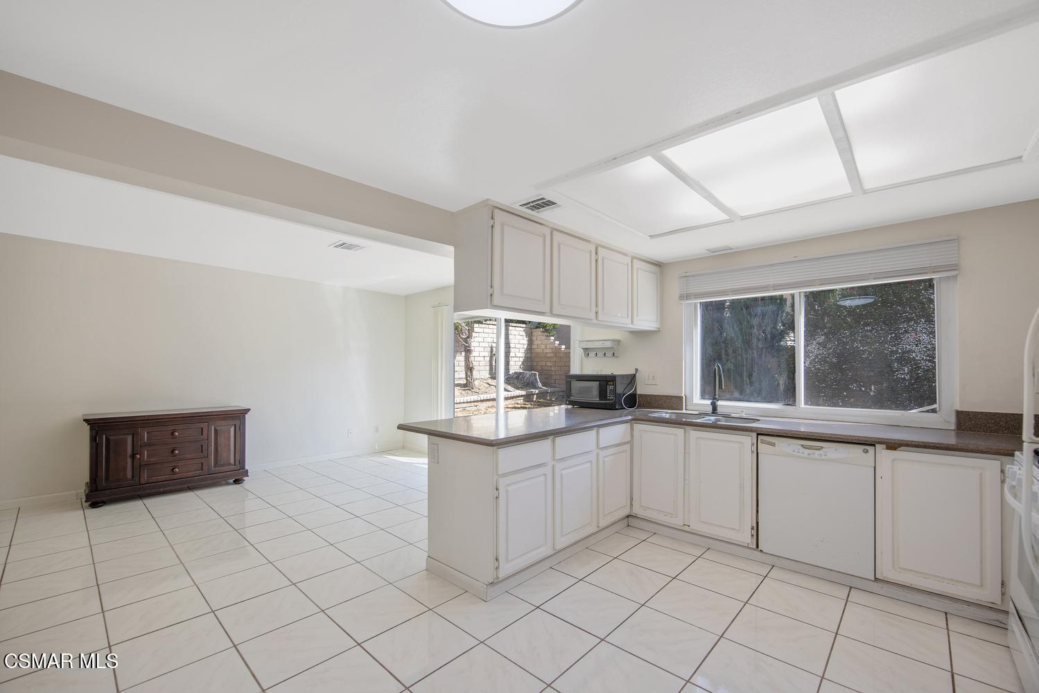 Kitchen with white cabinets, tiled floors, a peninsula counter, and a large window above the sink.