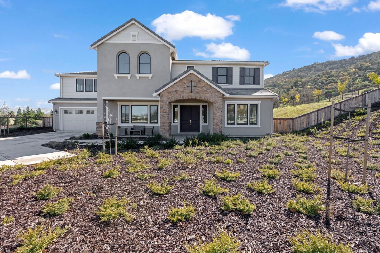 Two-story gray home with a stone entry, driveway, and landscaped hillside lot.