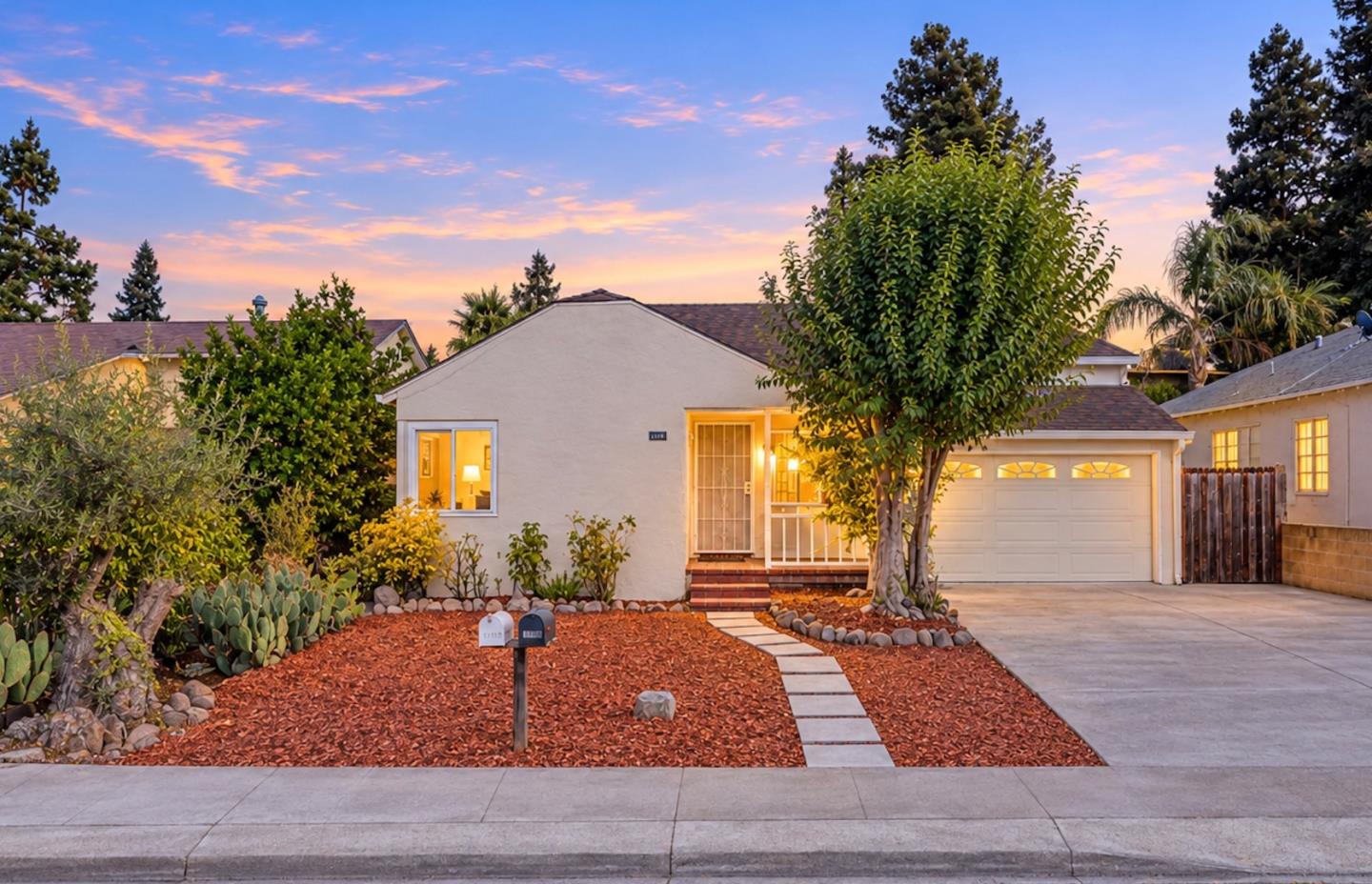 Single-story stucco home with an attached garage and landscaped front yard at dusk.