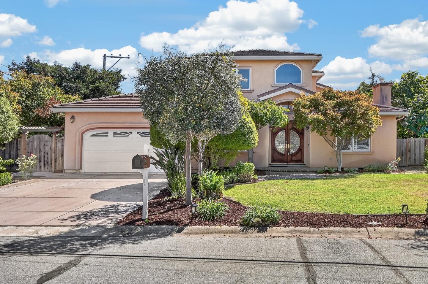 Two-story stucco house with arched wooden entry doors, a white garage door, and landscaped front yard.