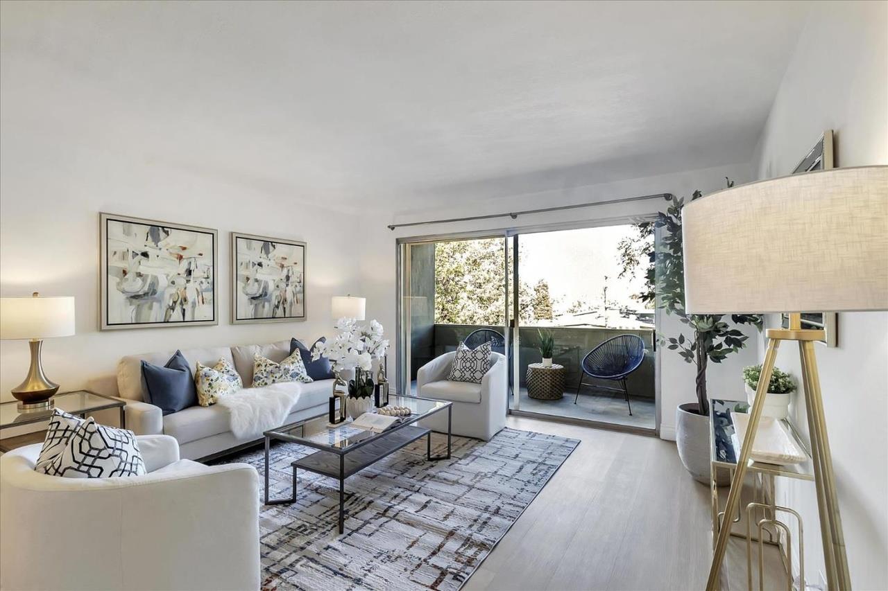 Staged living room with white sofas and sliding doors opening to a furnished balcony.