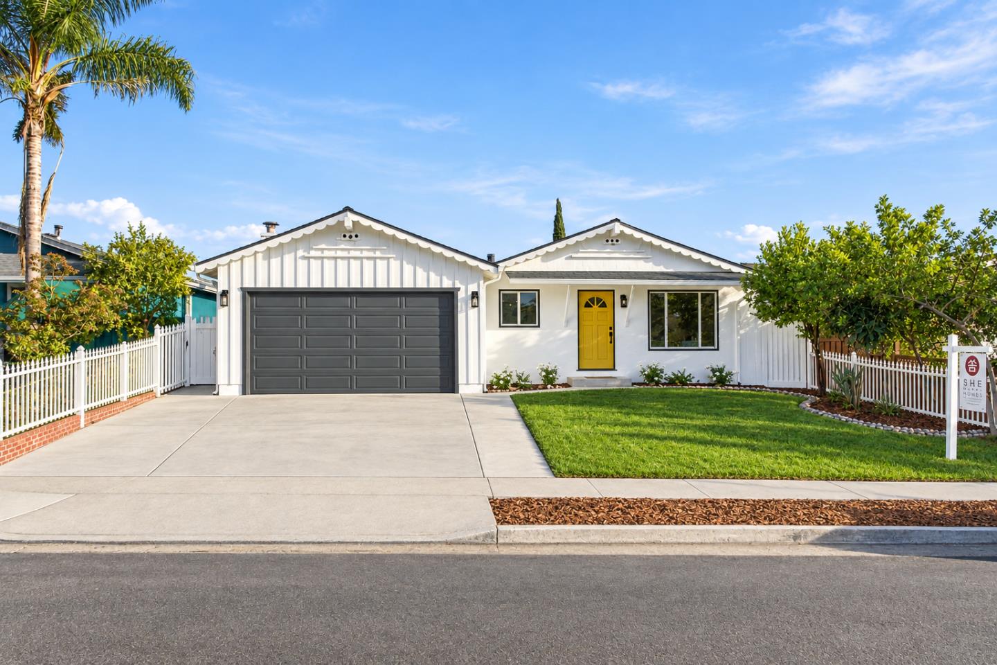White single-story home with a dark double garage, yellow front door, picket fence, and landscaped lawn.