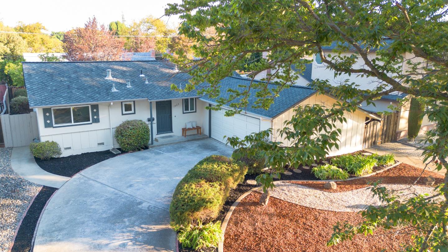 Single-story white house with an attached garage, curved driveway, and landscaped front yard beneath leafy trees.