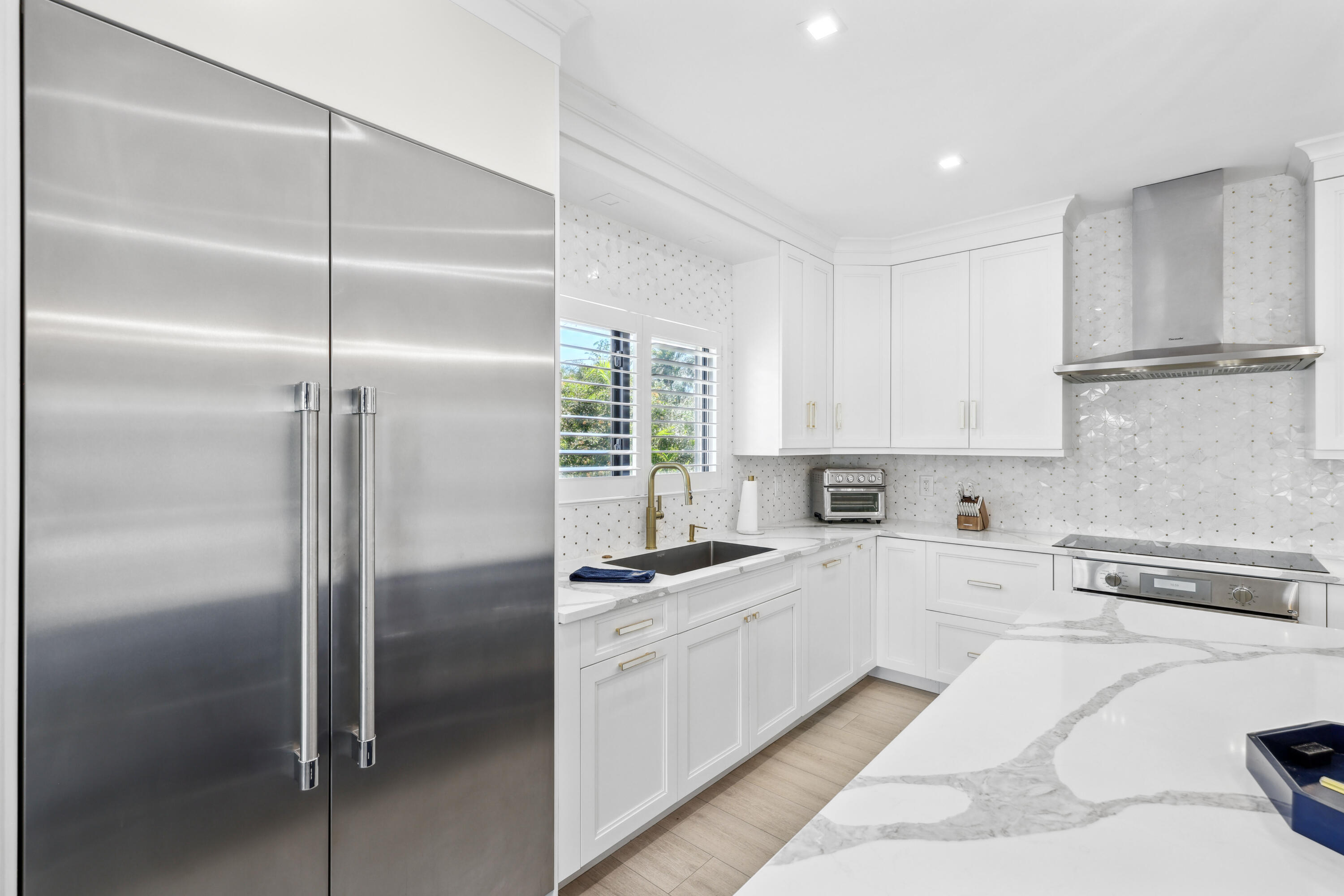 Bright white kitchen with a stainless steel refrigerator, marble island, and geometric tile backsplash.
