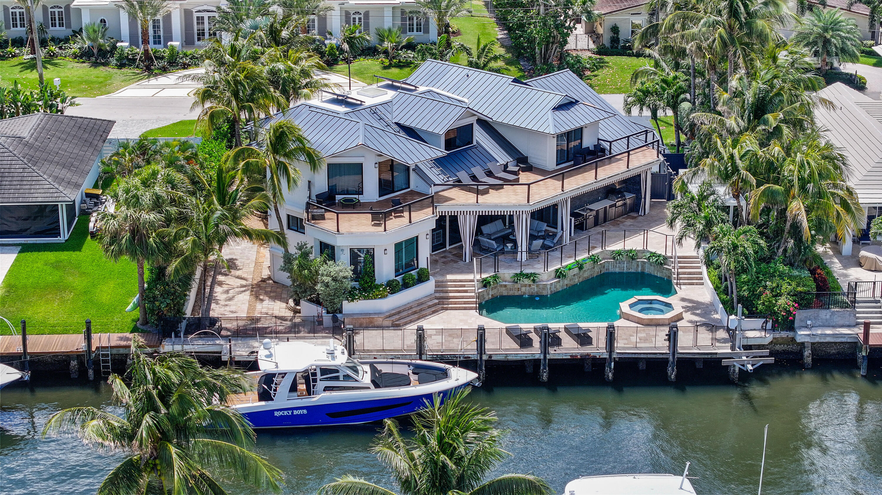 Aerial view of a waterfront home with a pool, wraparound terraces, and a boat docked on the canal.