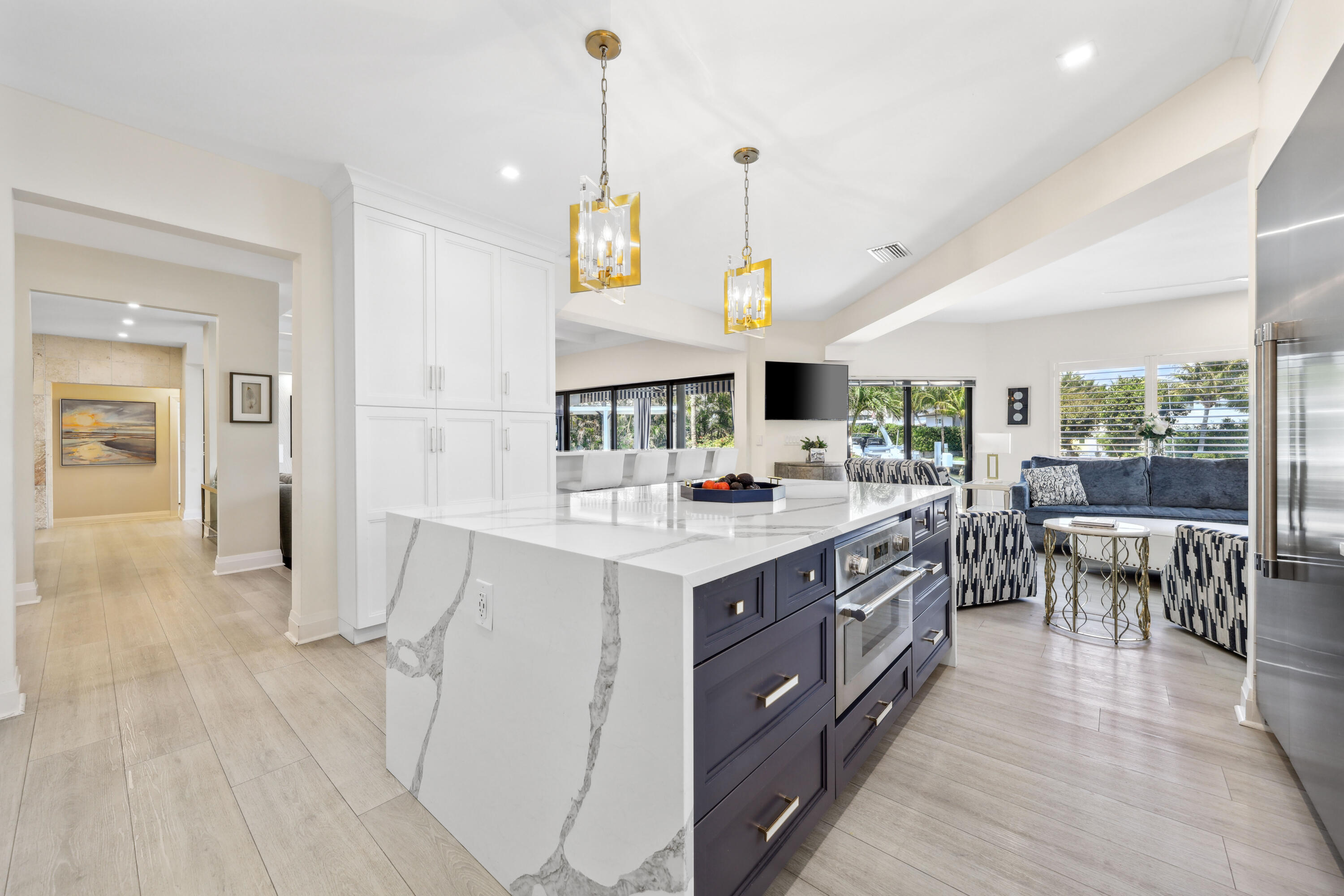 Open-plan kitchen with a veined stone island, navy cabinetry, gold pendants, and an adjoining sitting area.