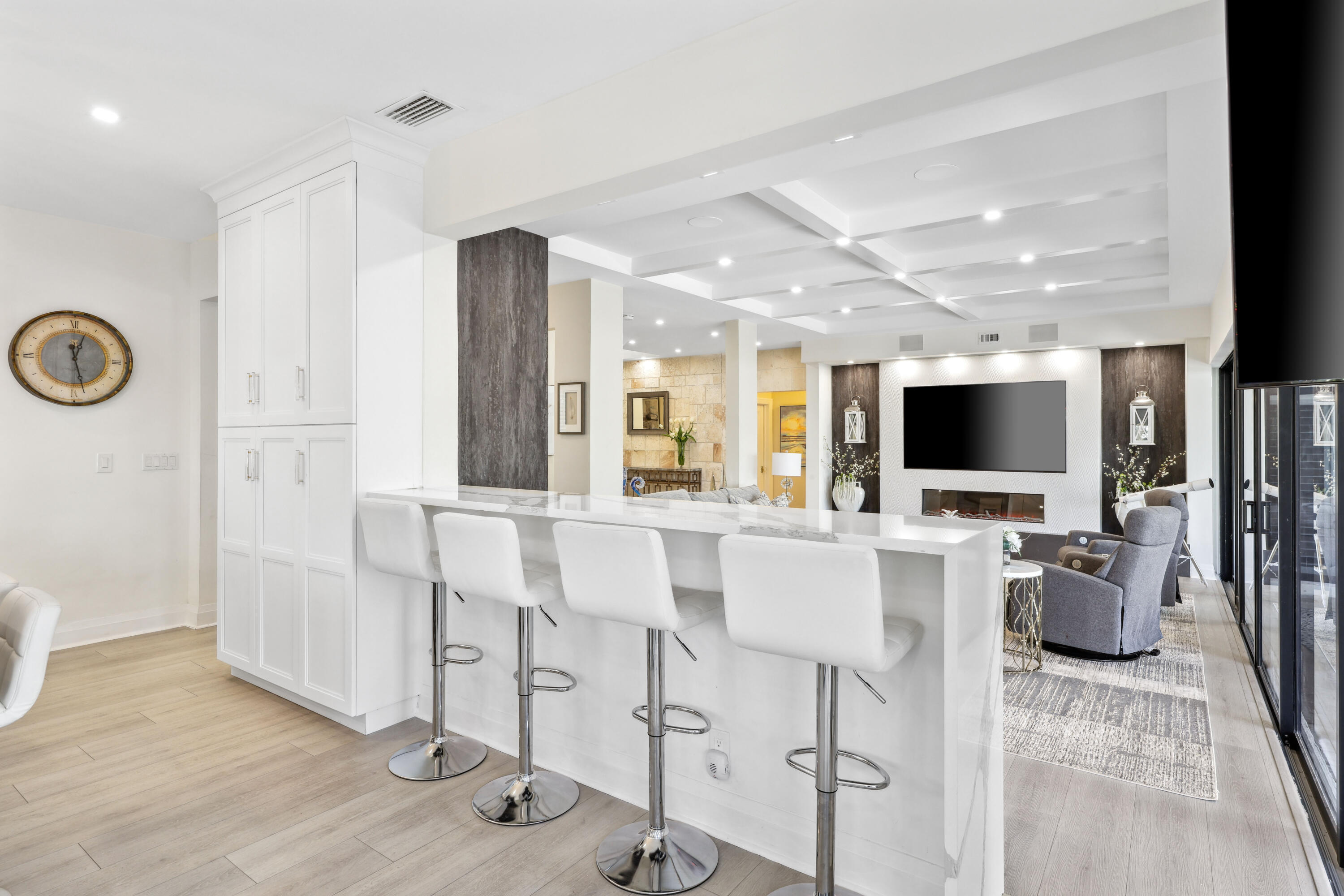 Open-plan kitchen and living room with a long white island and a fireplace beneath a mounted television.