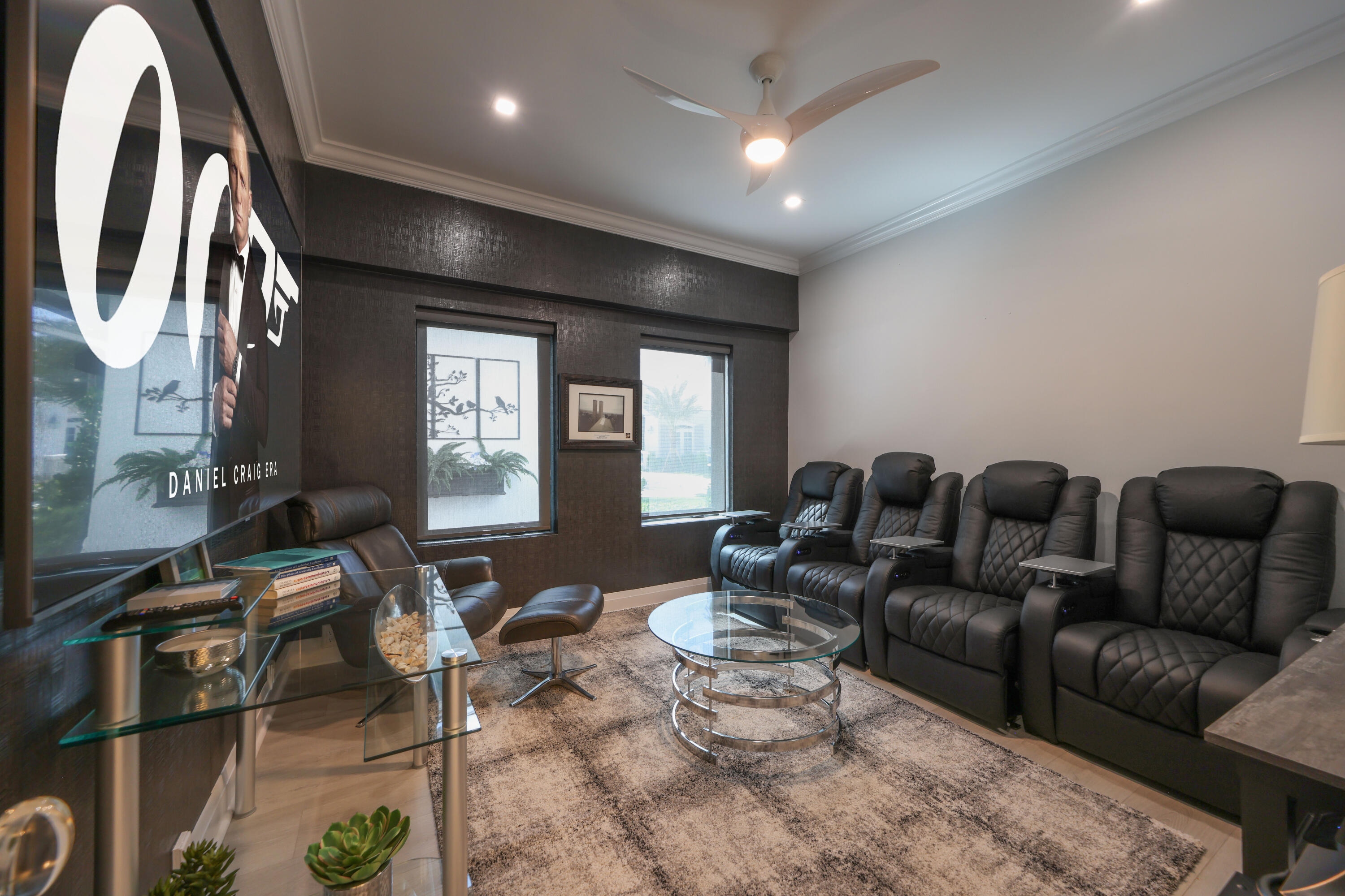 Home theater with black leather recliners, a large screen, and glass tables.