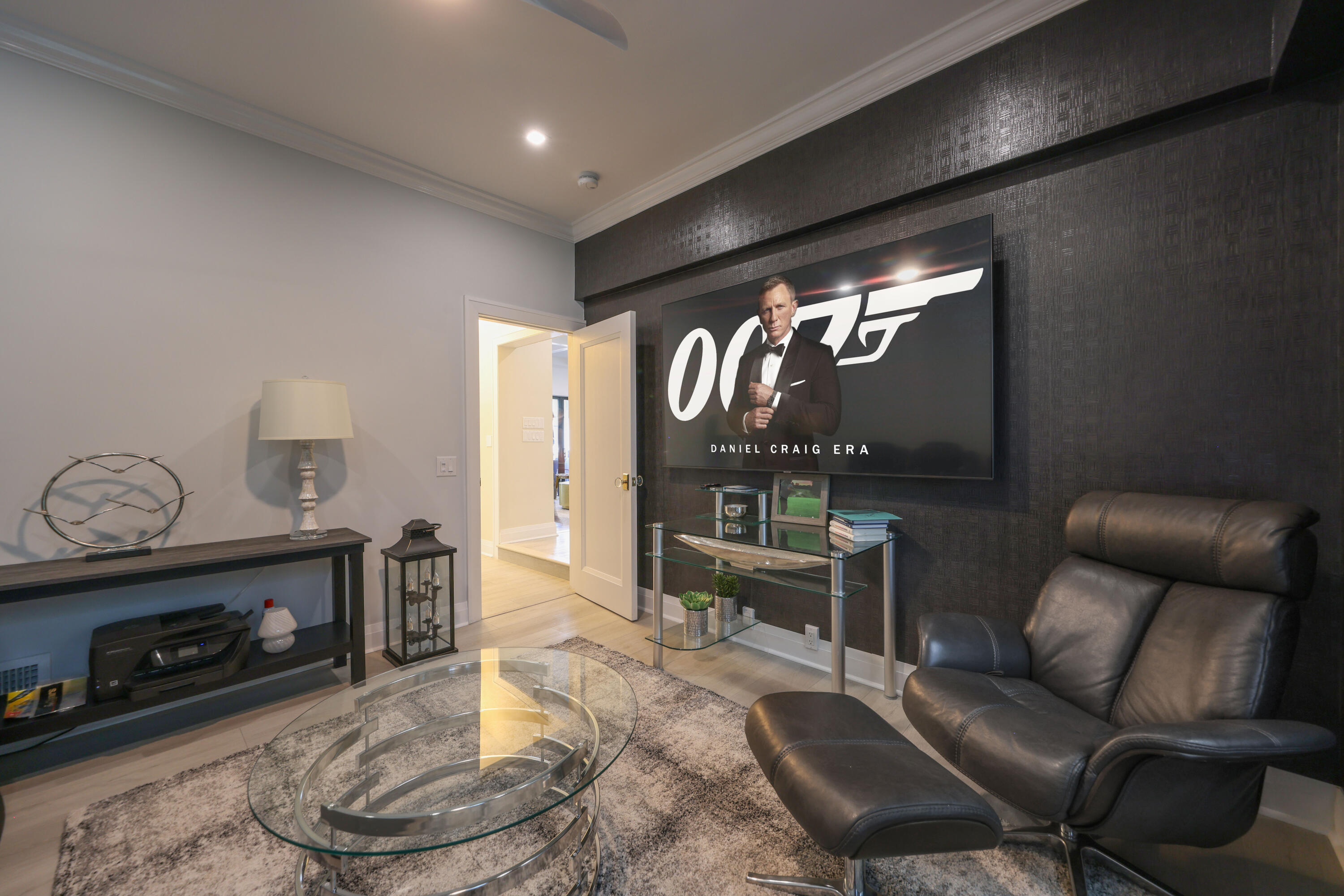 Furnished media room with a leather recliner, glass coffee table, and large James Bond poster.
