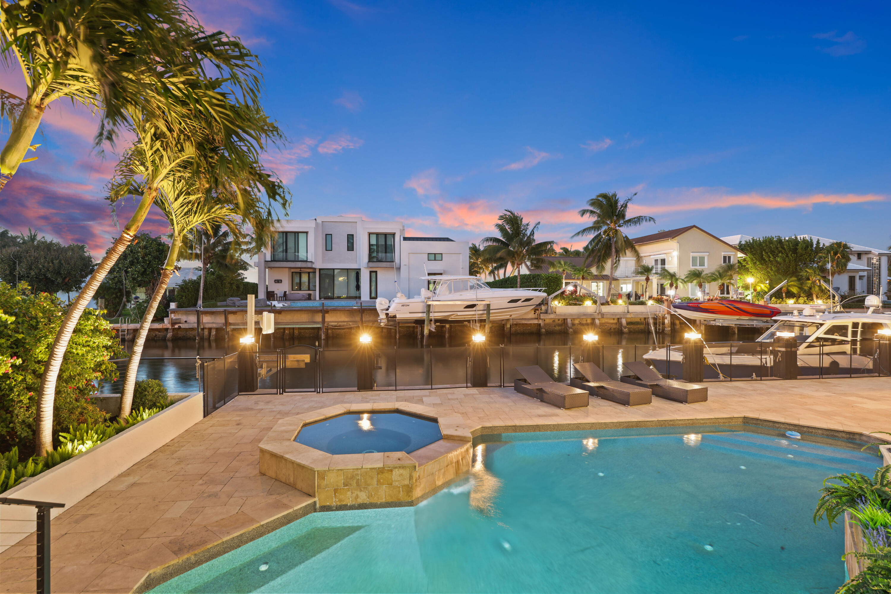 Waterfront home and dock behind a lit pool and spa at dusk.