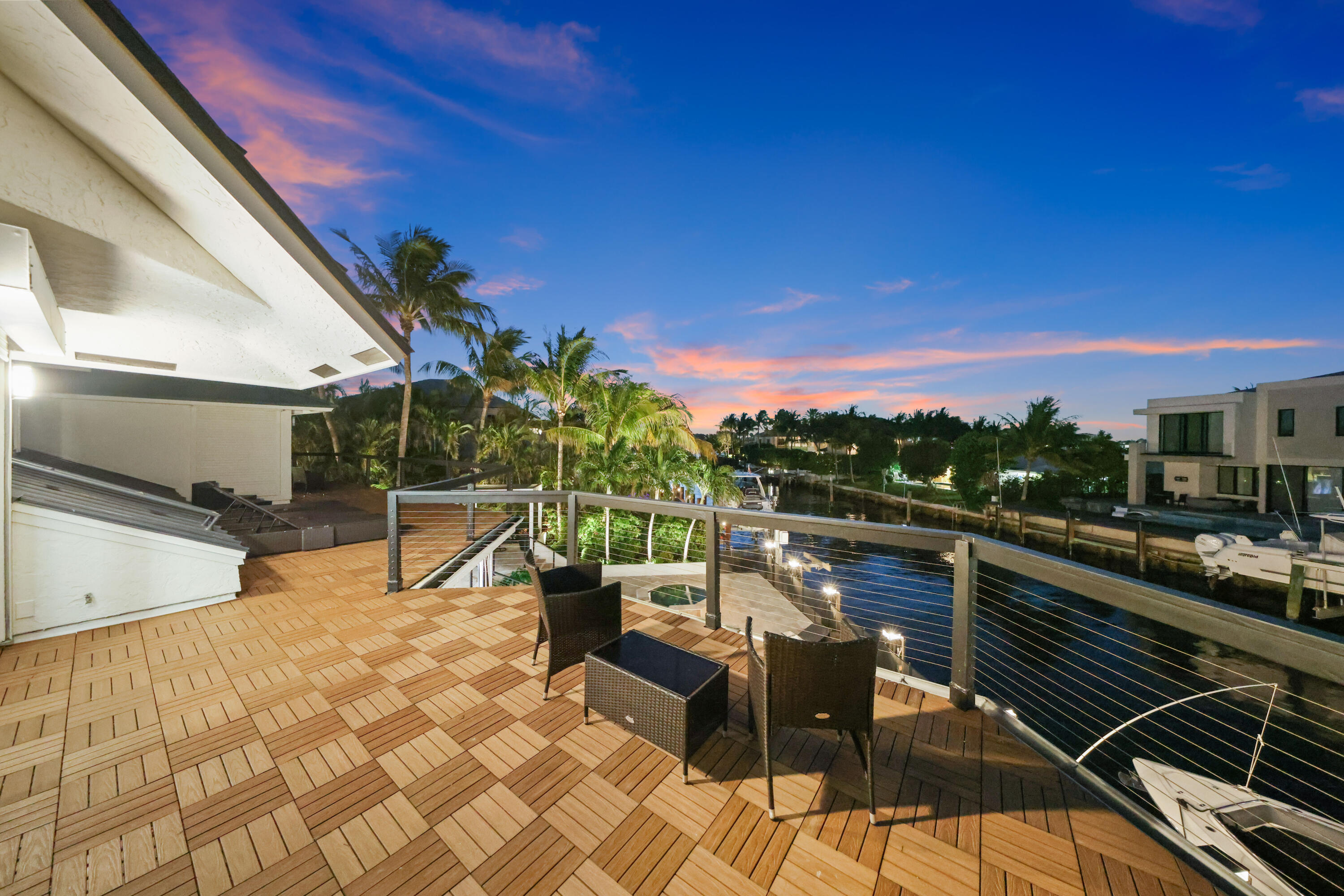 Waterfront deck with wicker seating, cable railing, and canal views at dusk.
