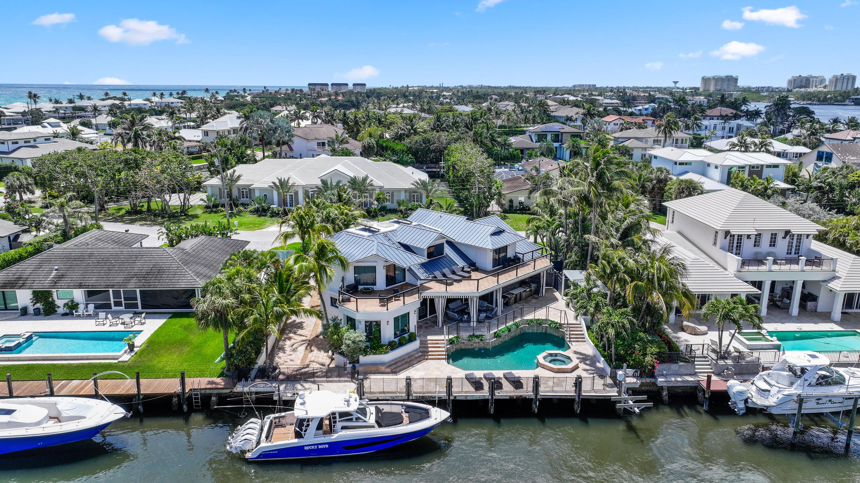 Waterfront home with a canal-side dock, swimming pool, and ocean visible beyond the neighborhood.