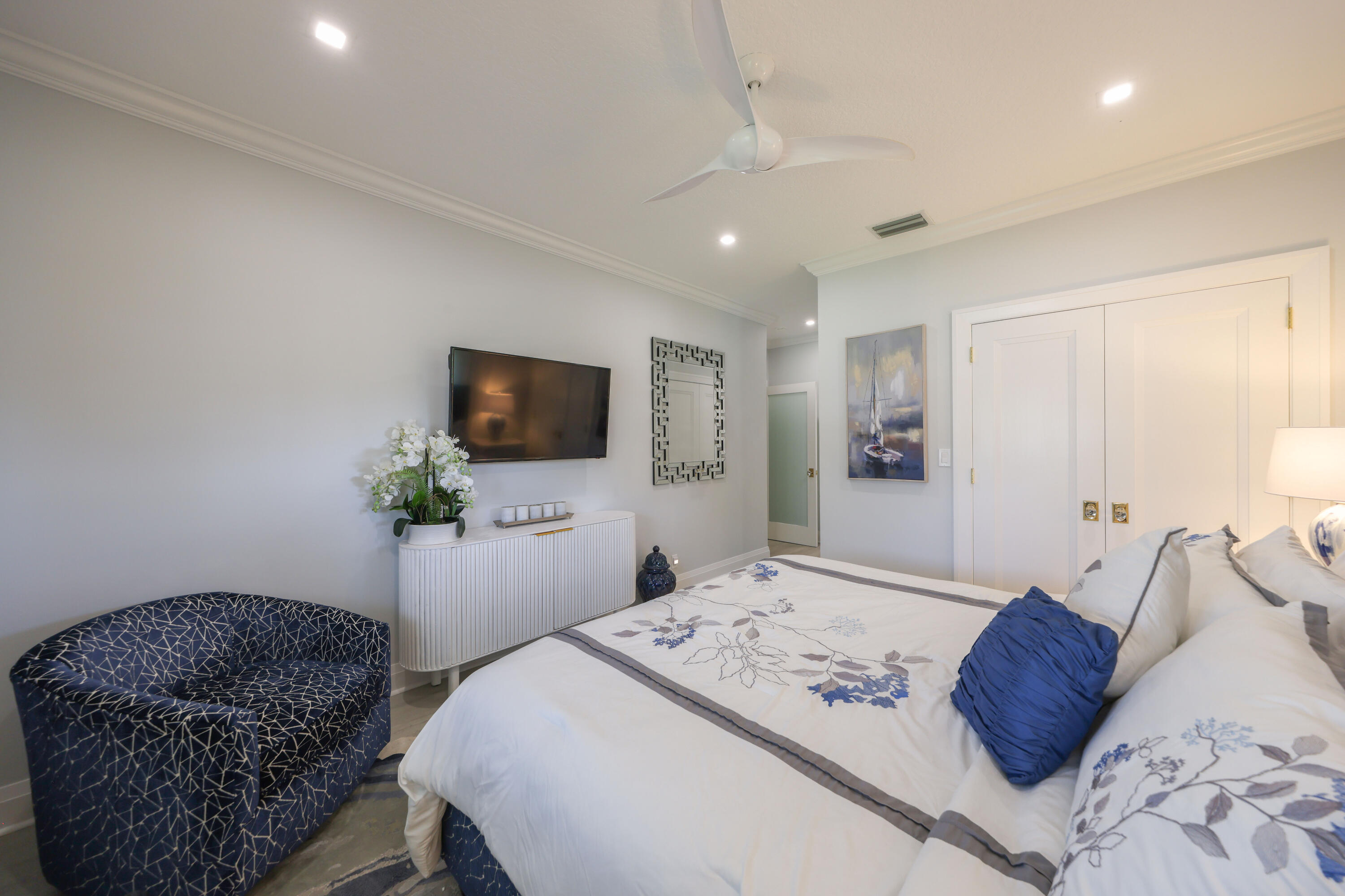 Bedroom with blue-and-white floral bedding, a navy patterned armchair, and a wall-mounted television.
