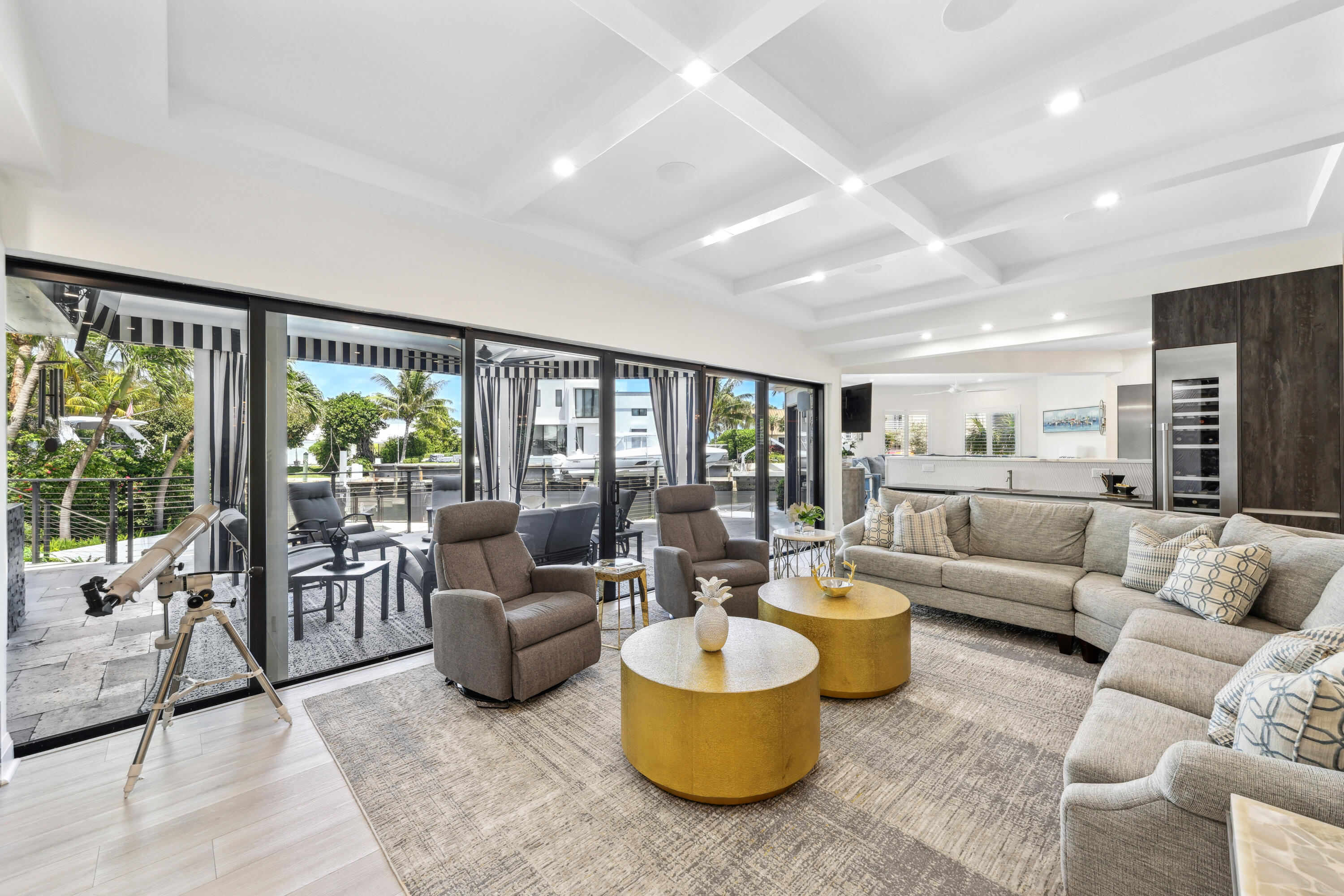Furnished living room with coffered ceiling, gold tables, and sliding doors overlooking a boat-lined canal.