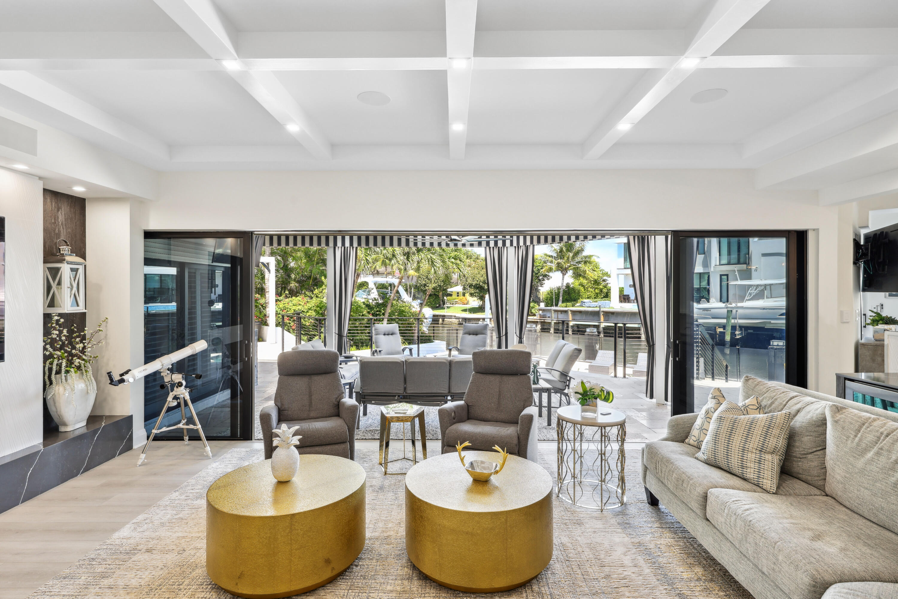 Living room with gold coffee tables and wide glass doors overlooking a canal and docked boat.