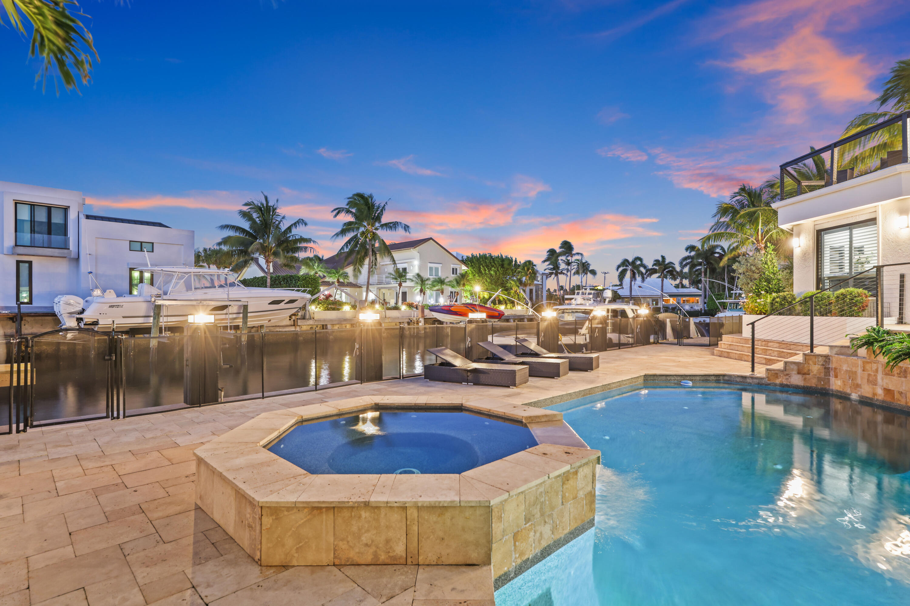 Waterfront pool and raised stone spa beside a canal with docked boats at dusk.