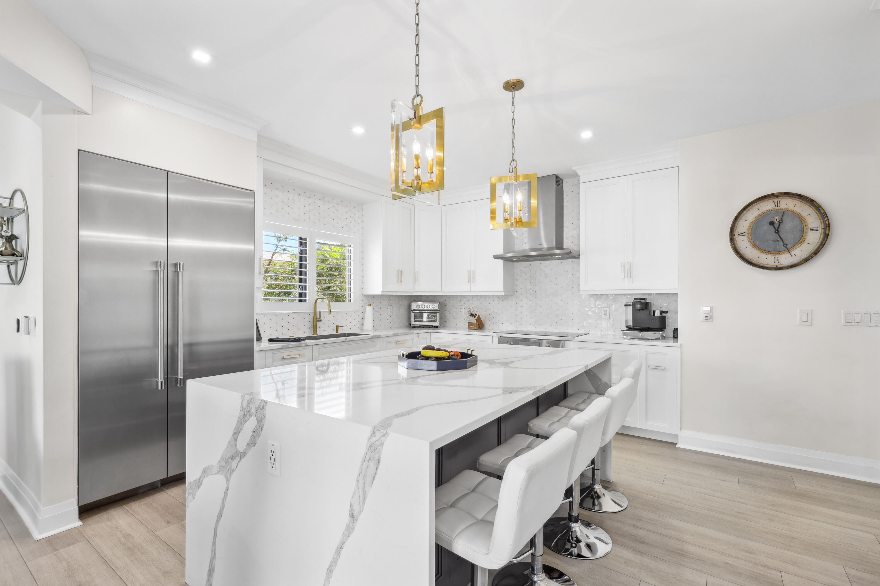 Bright white kitchen with a veined waterfall island, stainless steel appliances, and gold pendant lights.